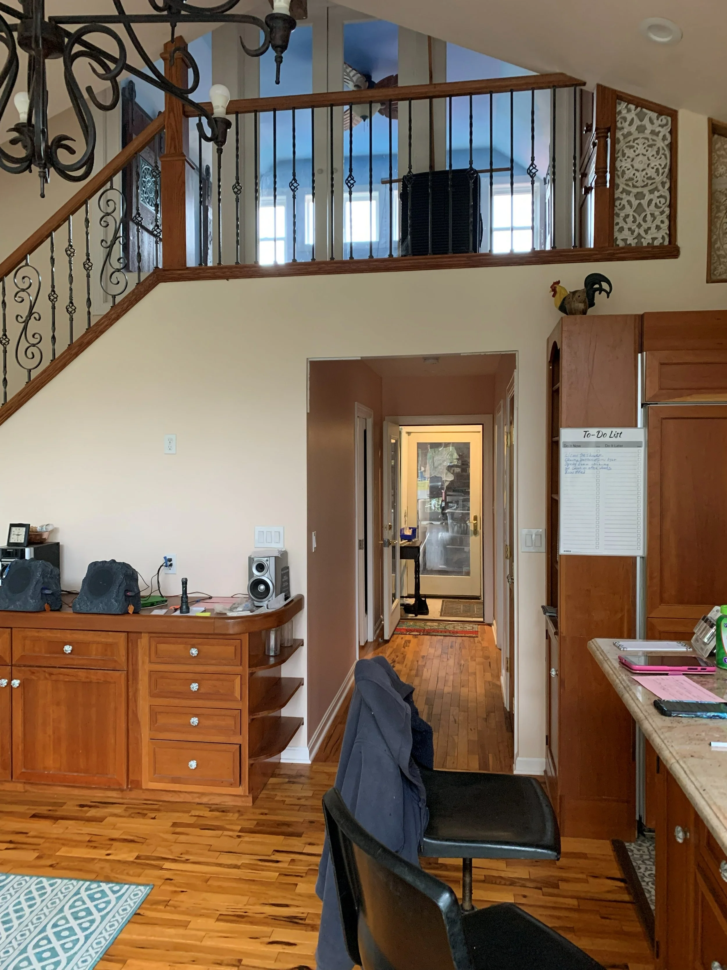 R.E. Arnold's Custom Construction. Living room with wooden floor and built-in wooden cabinet, staircase with decorative iron railing, and a chandelier hanging from the ceiling.