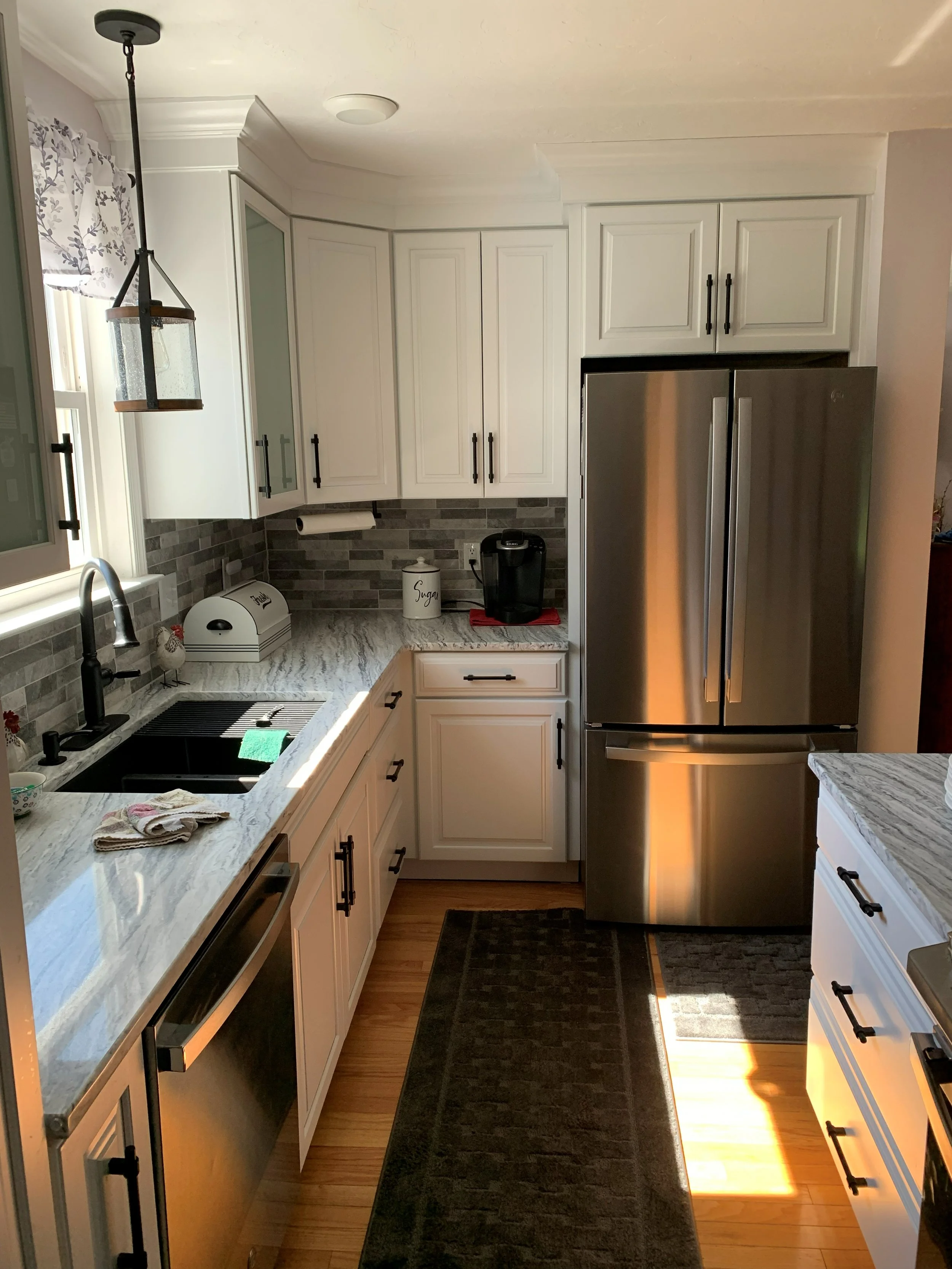 R.E. Arnold's Custom Construction. A modern kitchen with white cabinets, a stainless steel refrigerator, granite countertops, a black sink, and a tiled gray backsplash. 