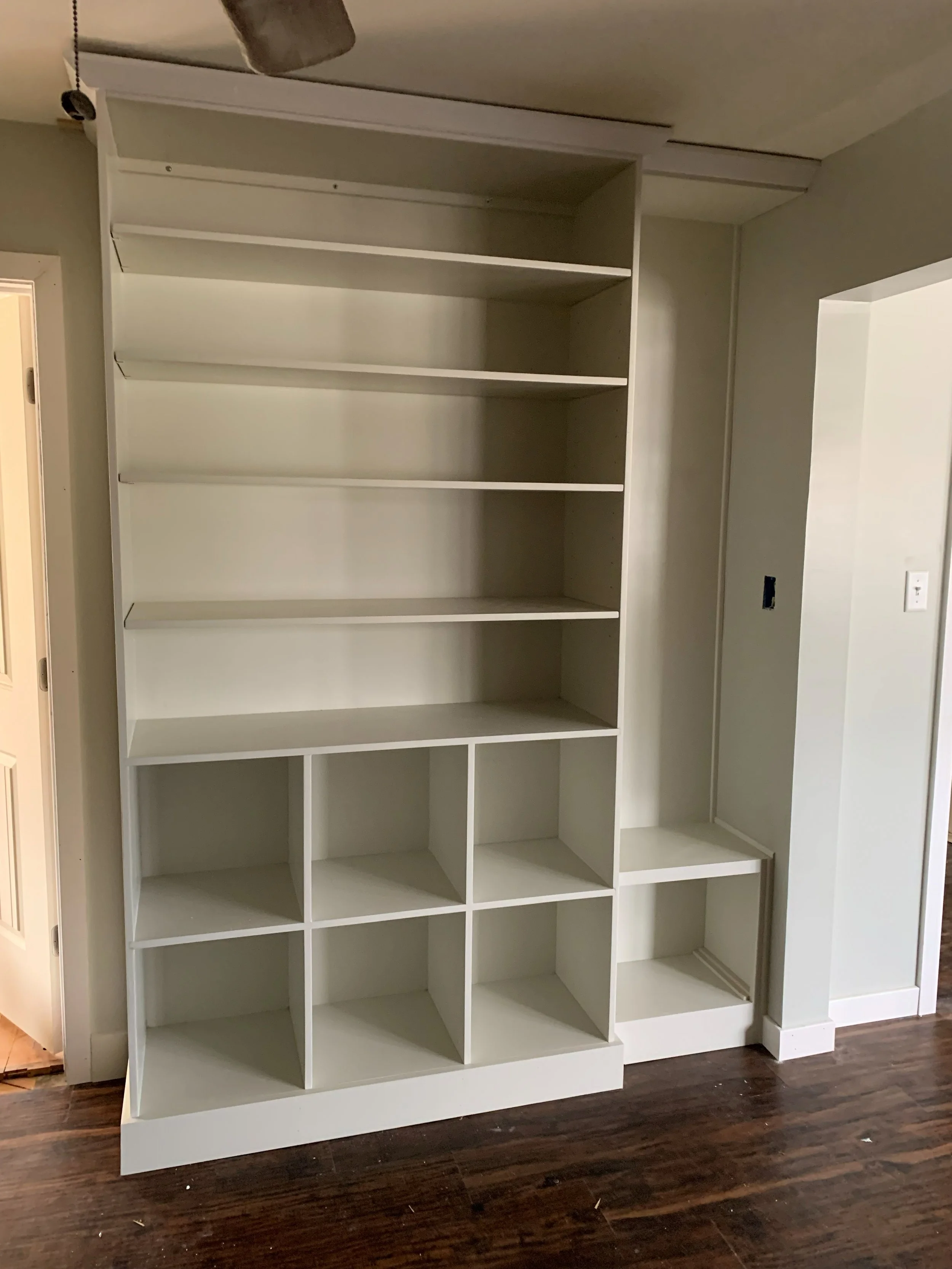 R.E. Arnold's Custom Construction. Empty white built-in bookshelf with multiple shelves and cubicles.