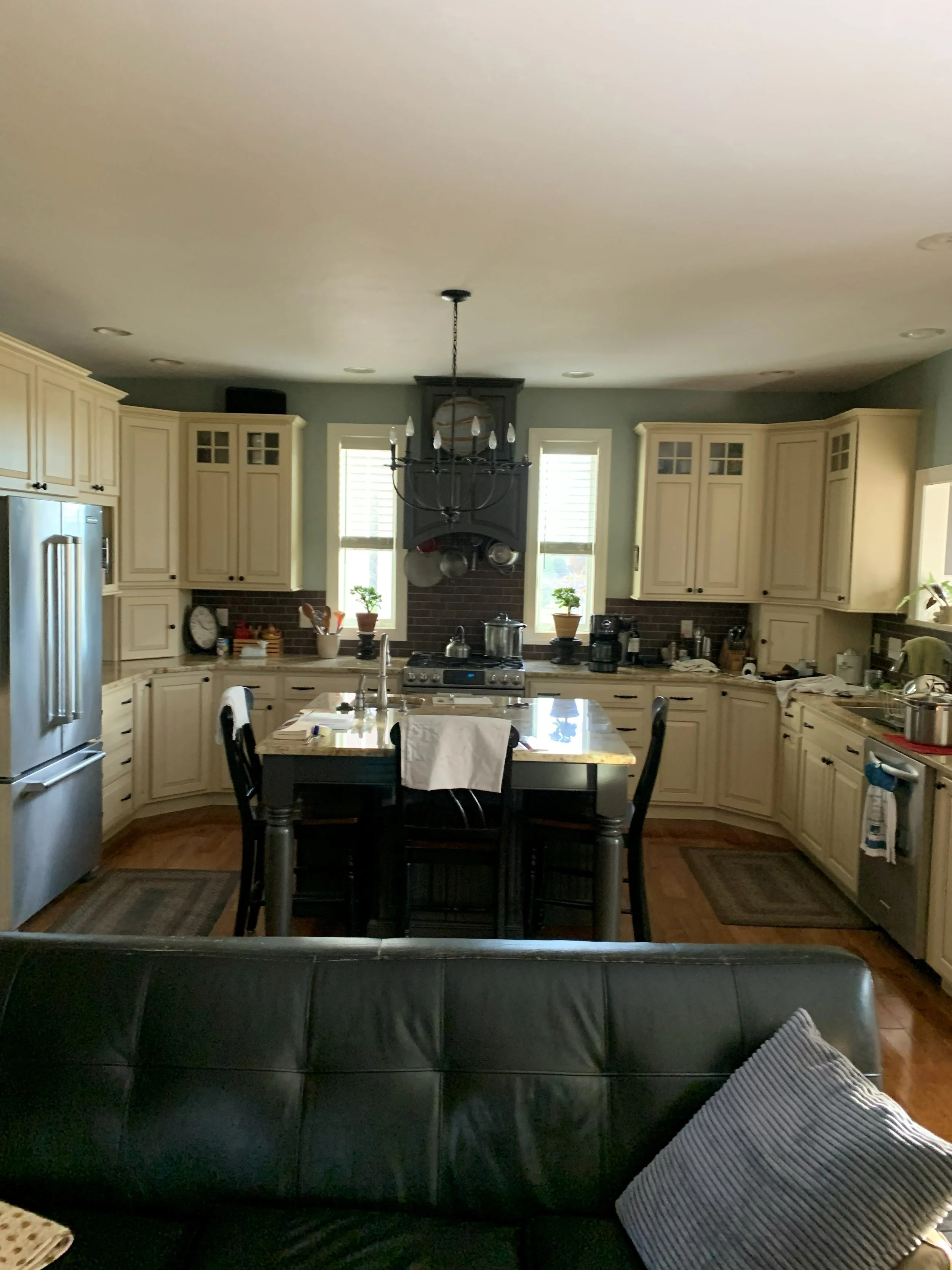R.E. Arnold's Custom Construction. Kitchen install with cream-colored cabinets, stainless steel refrigerator, black chandelier, and a central island with seating.