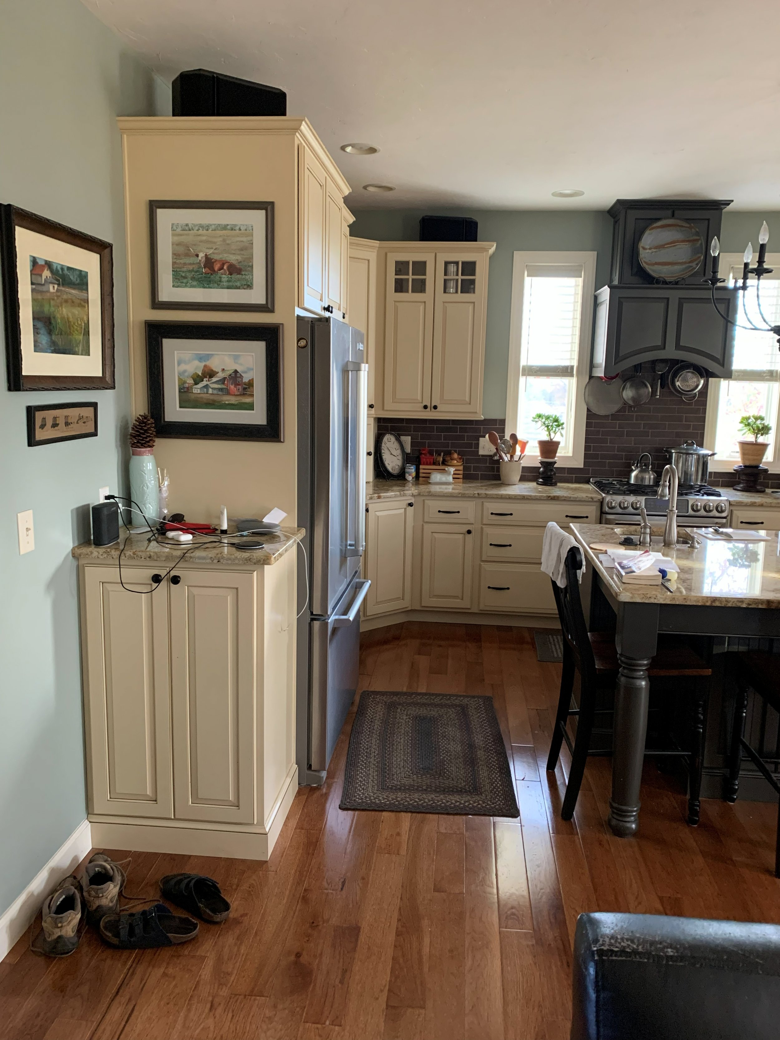R.E. Arnold's Custom Construction. A kitchen install with cream-colored cabinets, a stainless steel refrigerator, a black range hood, and a kitchen island. 