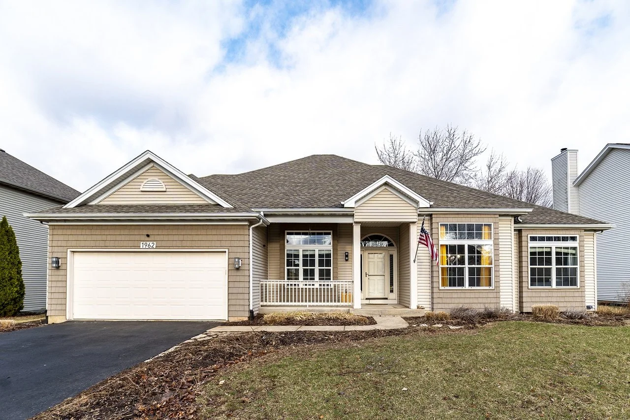Front view of a beige house with a two-car garage, a small front porch, and a lawn.