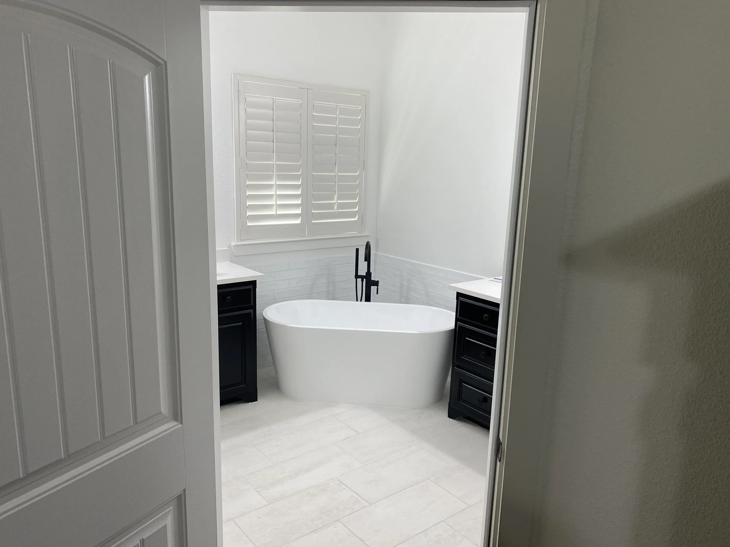 Freestanding Tub & Floor-Mount Faucet Bathroom Design – McKinney, TX. Modern bathroom featuring a standalone soaking tub with a floor-mounted faucet, complemented by light porcelain tile flooring and classic subway tile accents.