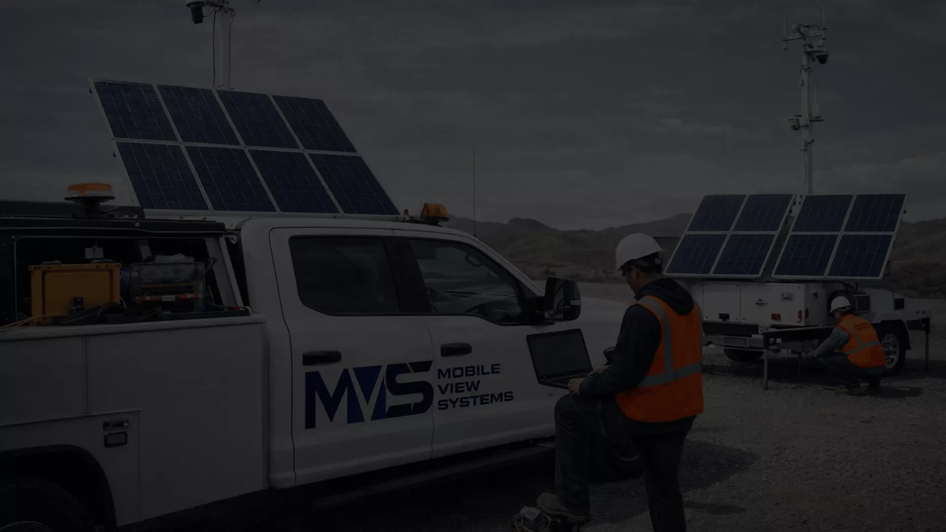 Technician setting up a solar-powered mobile surveillance trailer with mountains in the background.