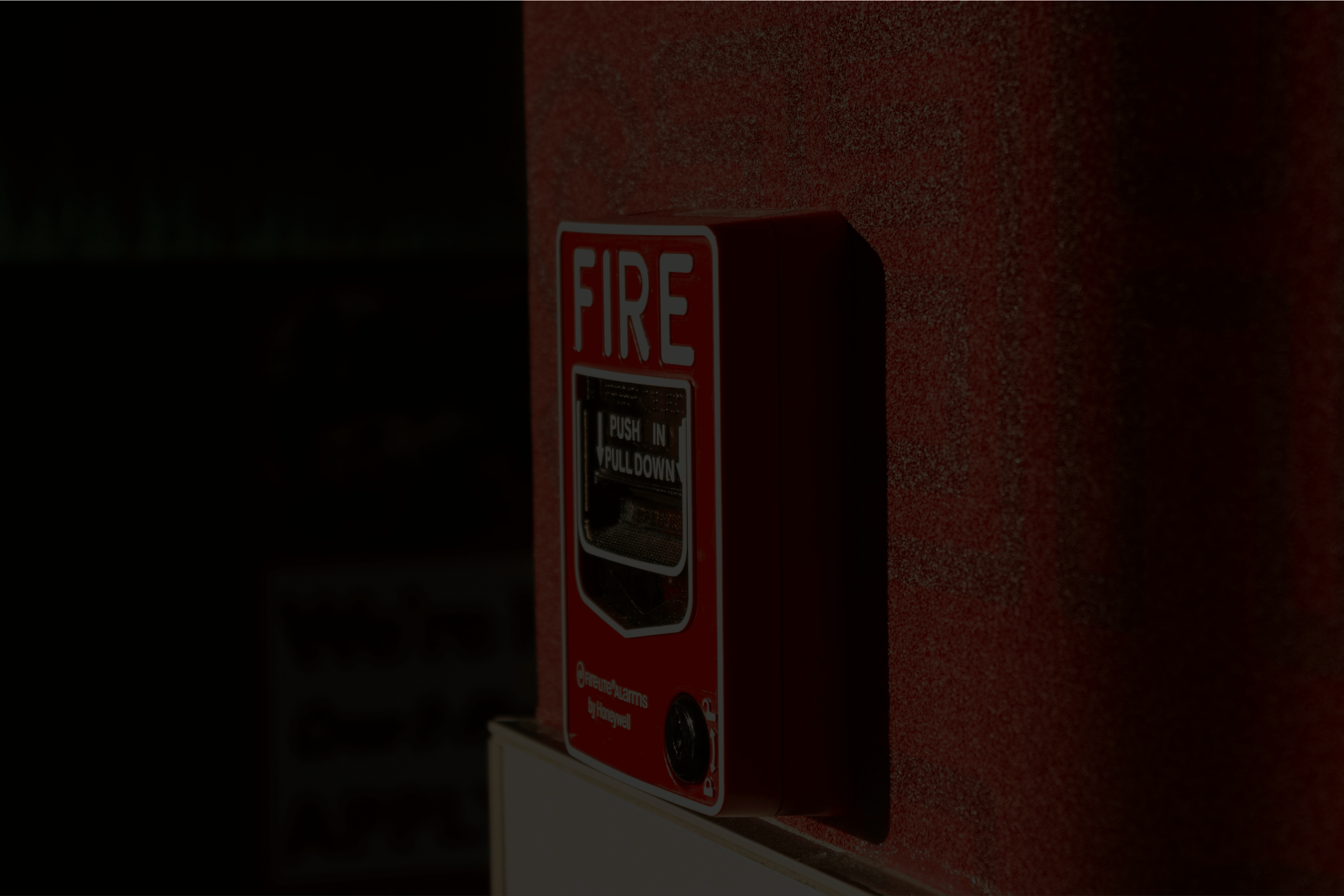 A red fire alarm pull station mounted on a red textured wall.