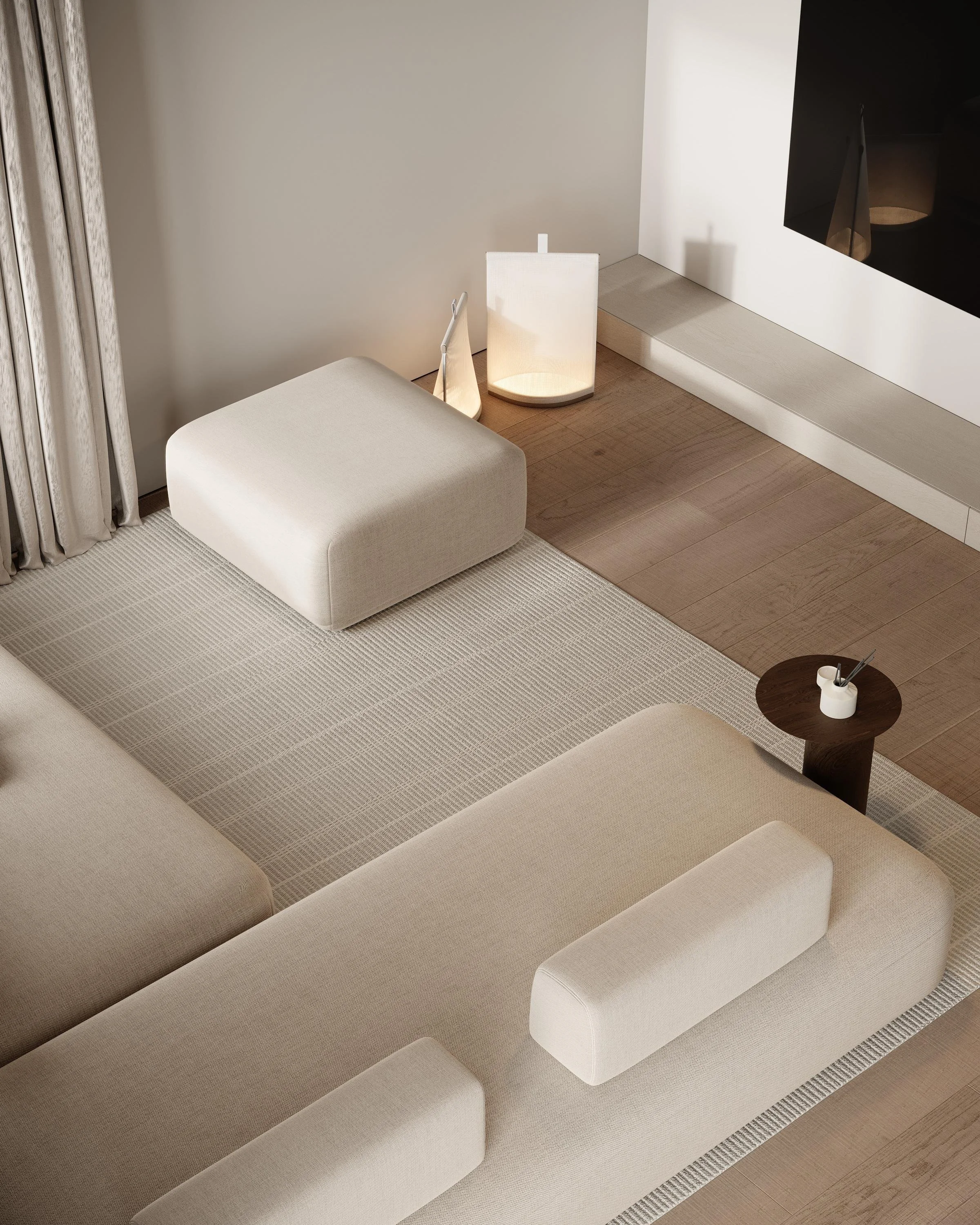 A modern living room corner with a beige sectional sofa, a small round wooden side table, a white ottoman, a floor lamp, and a TV mounted on the wall.