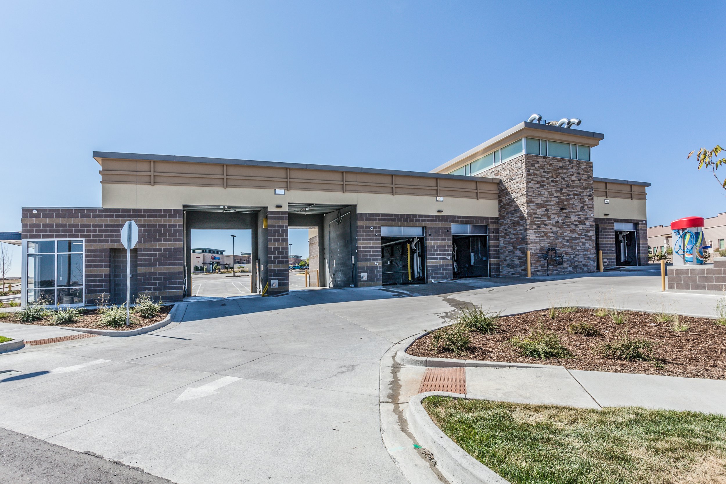 Empty drive-thru building at a fast food restaurant with a brick facade, large windows, and a small landscaped area in the foreground.