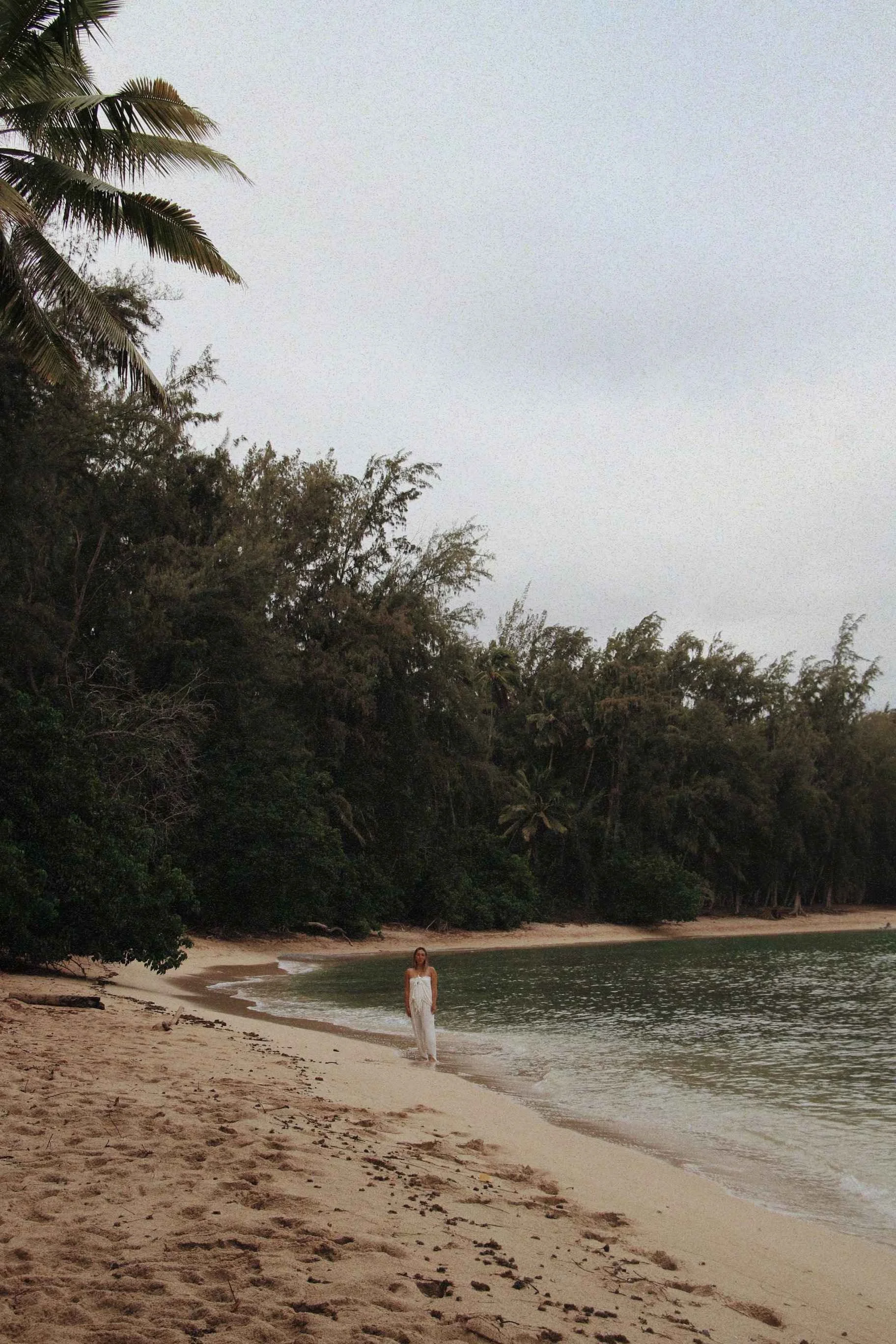 A photo of a woman standing on the shoreline of a tropical beach