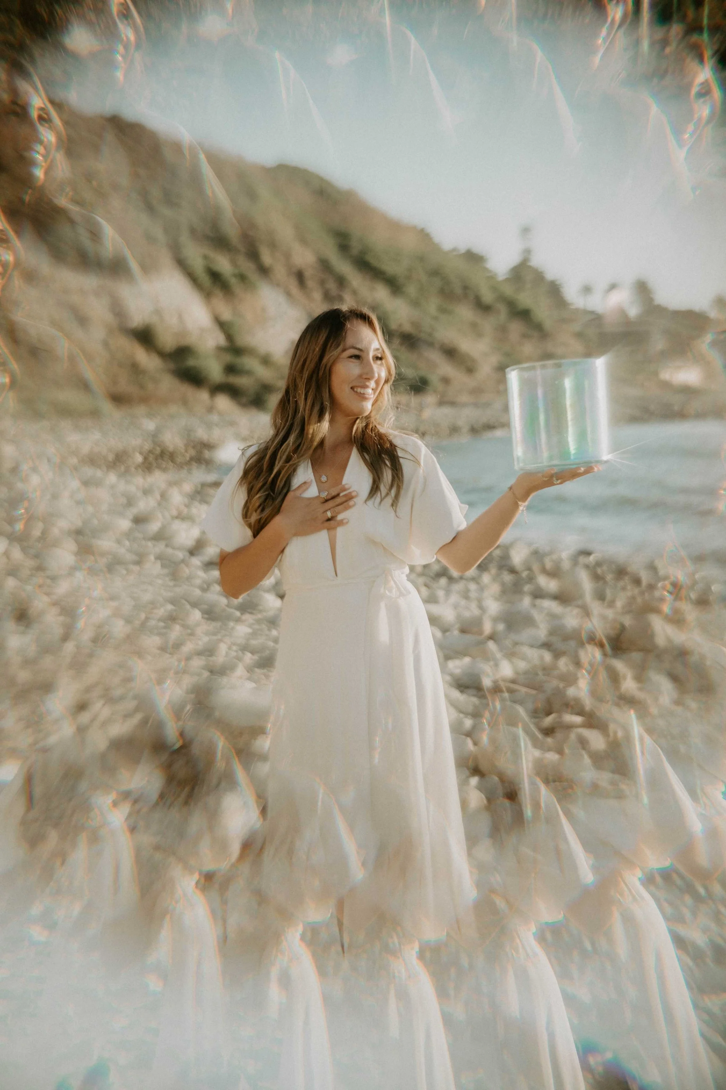 An artistic photo of Sophie Pyne holding an iridescent sound healing bowl on the beach