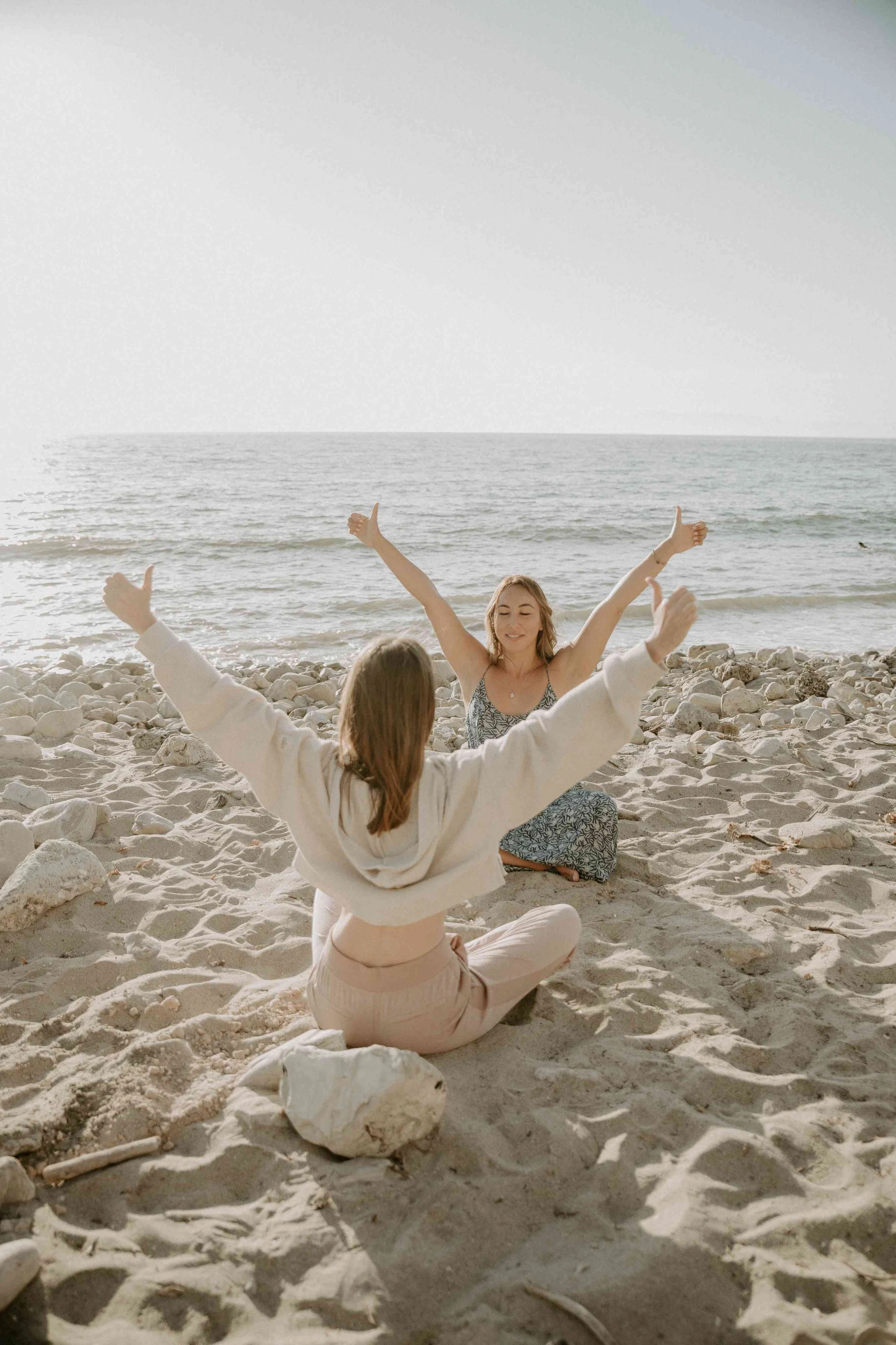 Sophie Pyne and her friend sitting on the sand at the beach facing each other while stretching their arms in the air