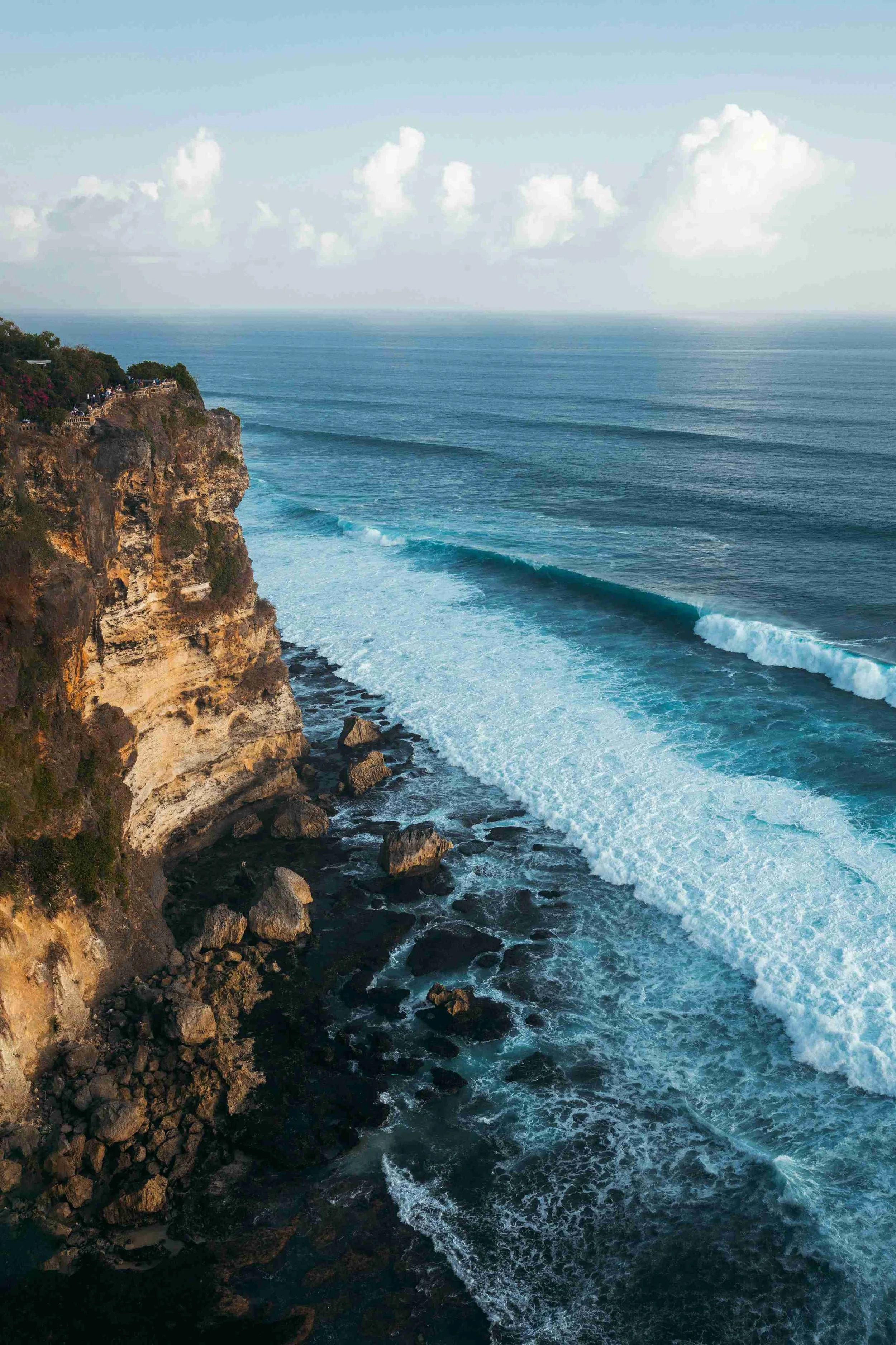 An aerial view photo of the bright blue ocean water crashing against the cliffs