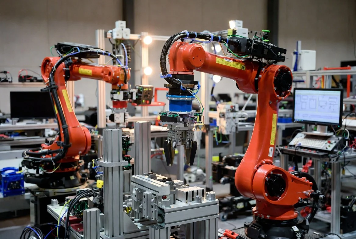 Two orange industrial robotic arms are working together to assemble for Resarch and Development Materials and Components, in the Tektite Genome Robotics Division laboratory.