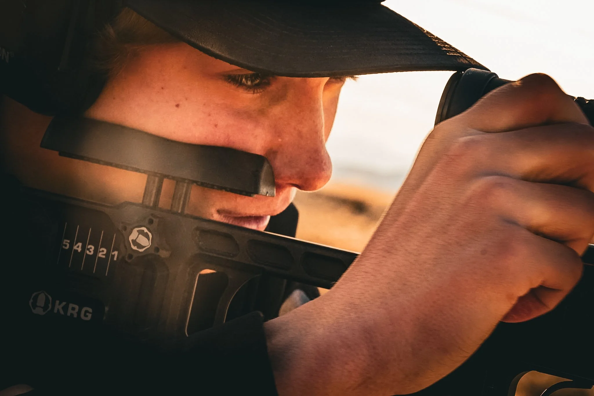 Close-up of a person inspecting a rifle, wearing tactical gear and a helmet, focusing on their face and hand holding the firearm.