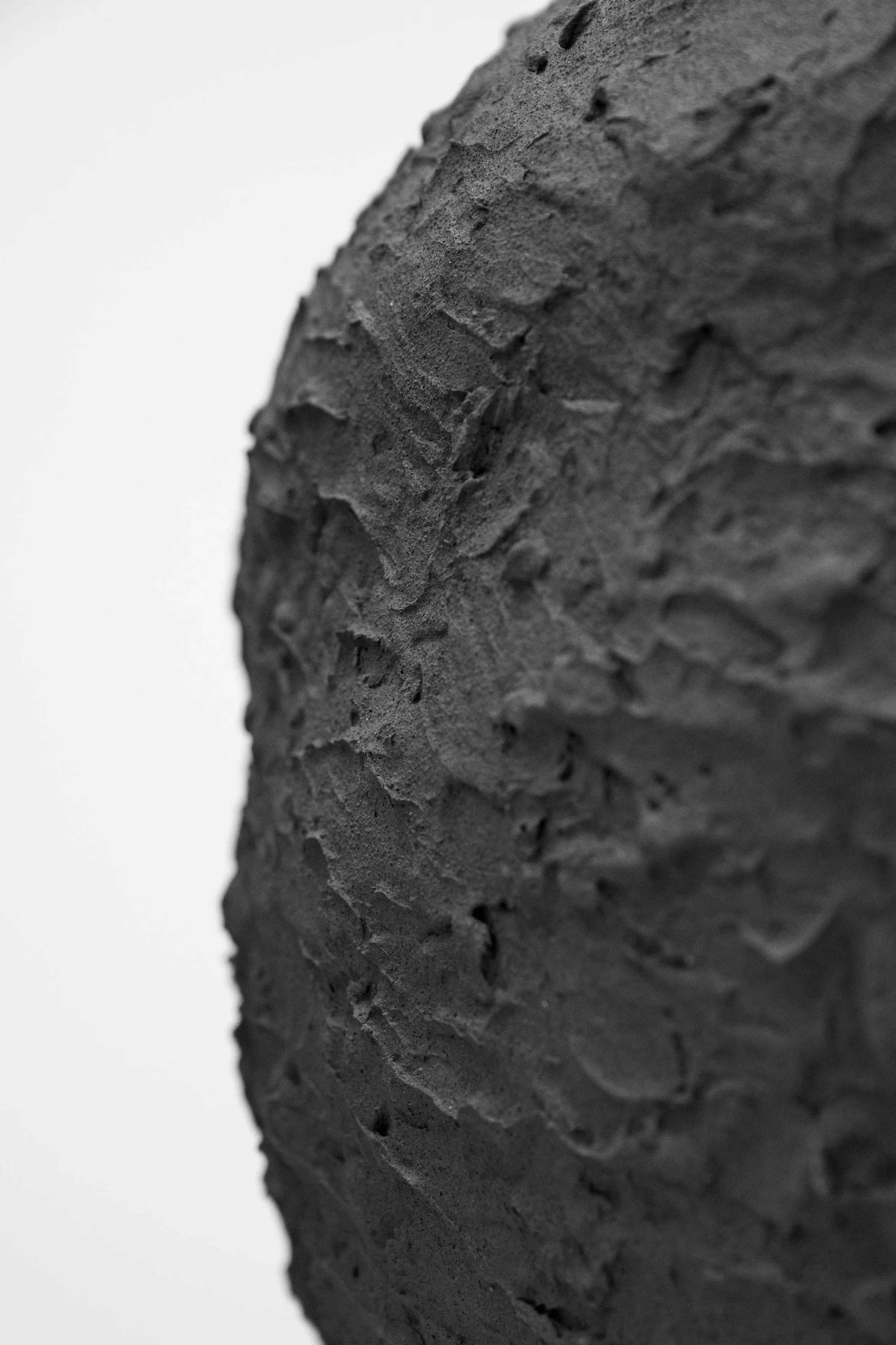 Close-up of a rough, textured, black rock surface against a plain white background.