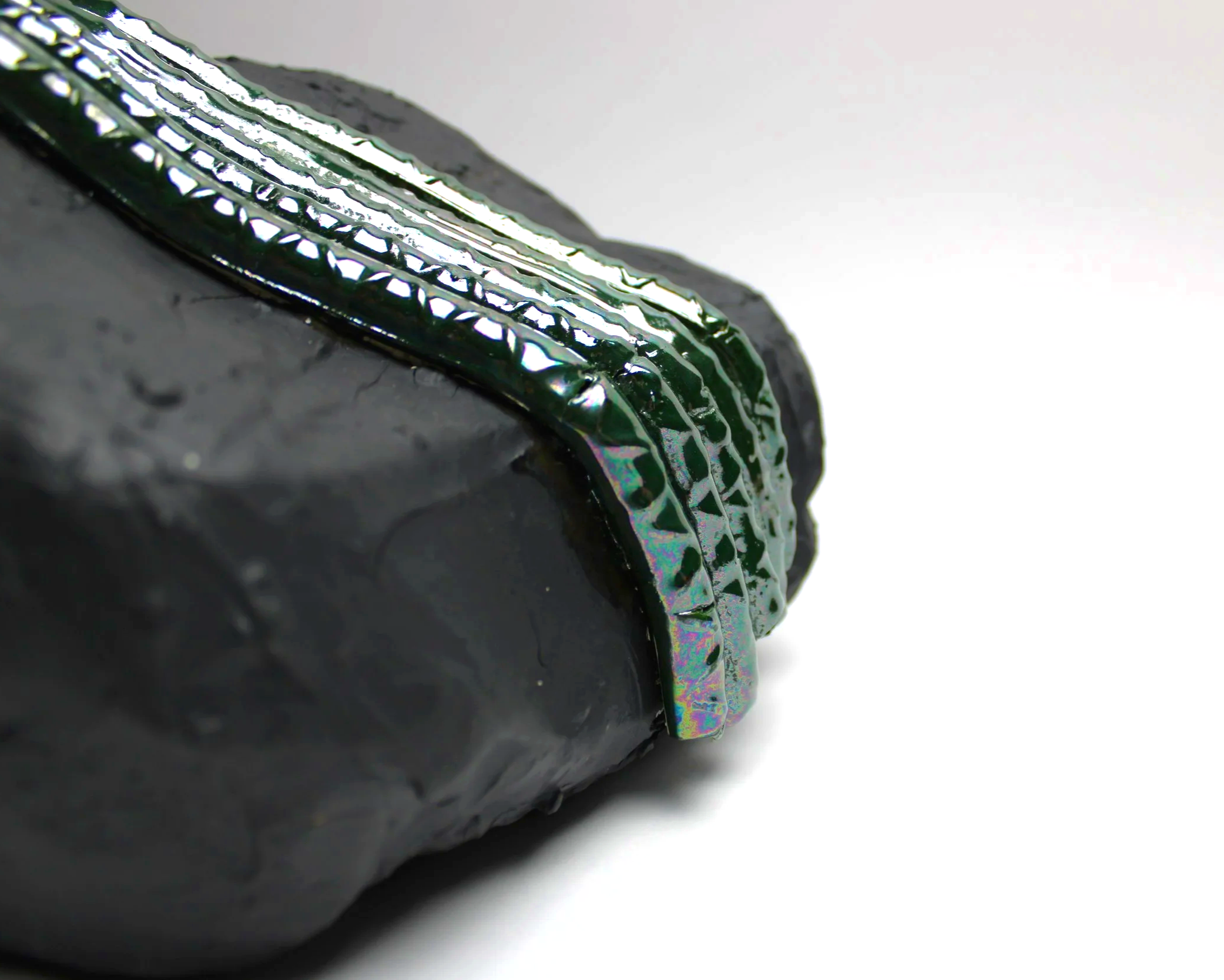Close-up of a broken black ceramic sculpture with jagged edges and colorful iridescent glaze on a white background.