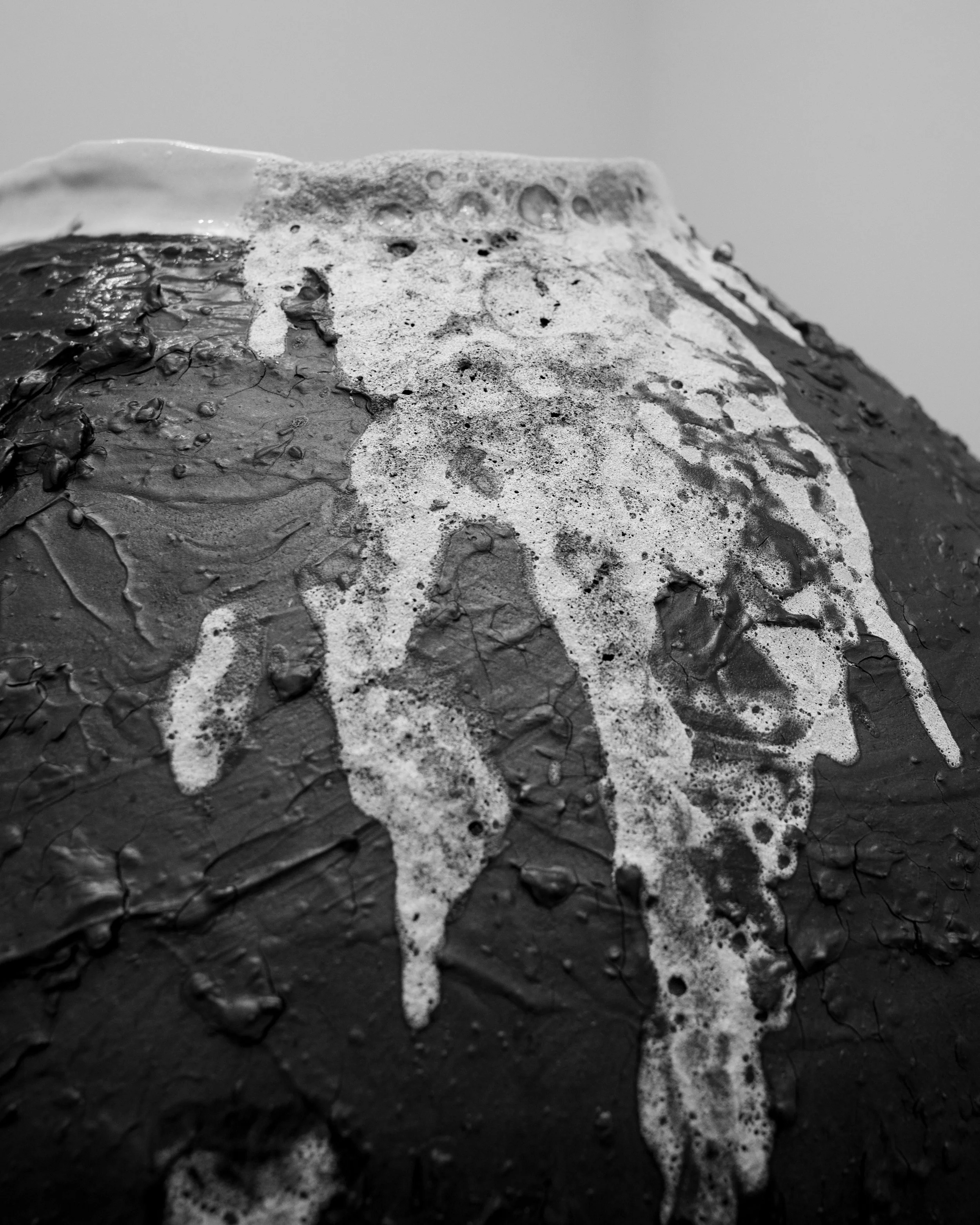 Close-up black-and-white photo of lava glaze on a textured surface, possibly wet asphalt or concrete.