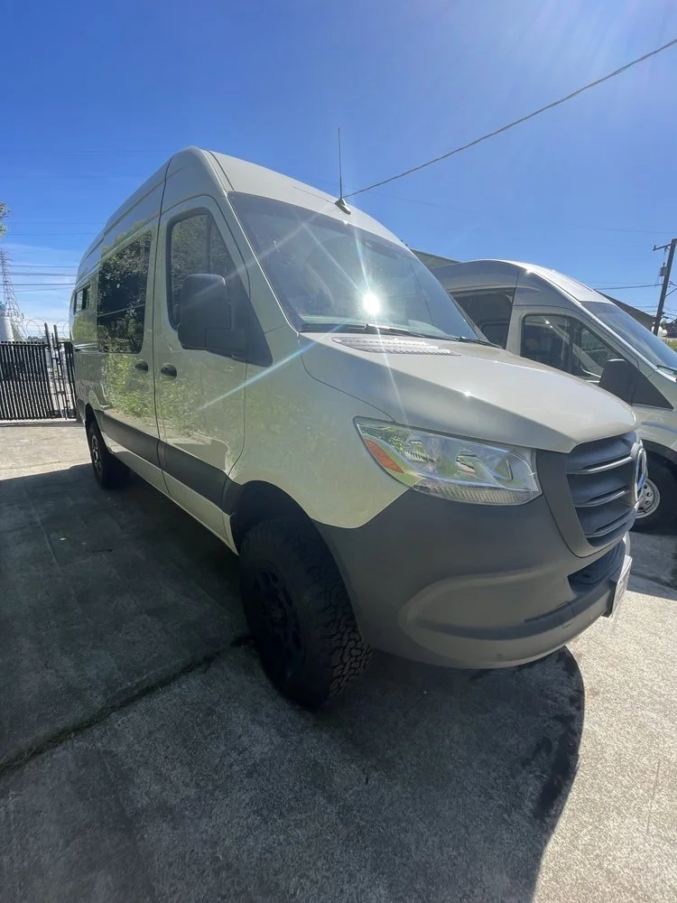 A white cargo van parked on a concrete surface under a clear blue sky.