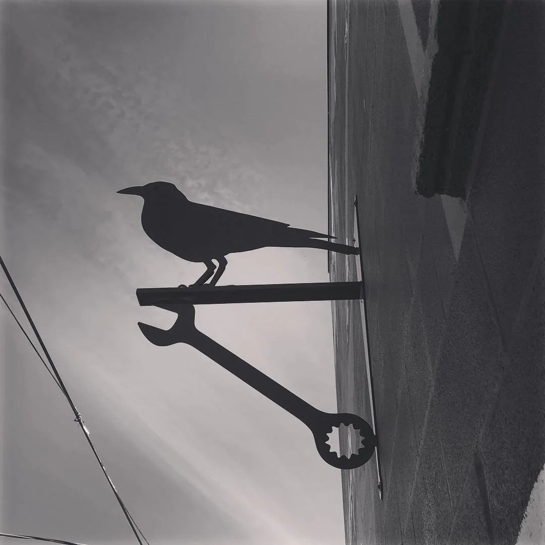 Silhouette of a bird perched on a large wrench on a rooftop, with the ocean and sky in the background.