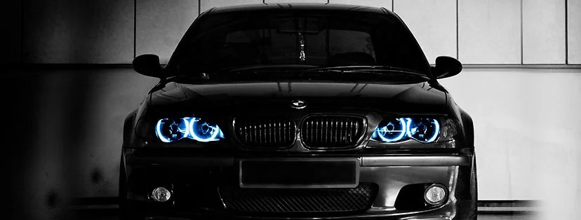 Black BMW car with illuminated blue headlights in a dark garage.