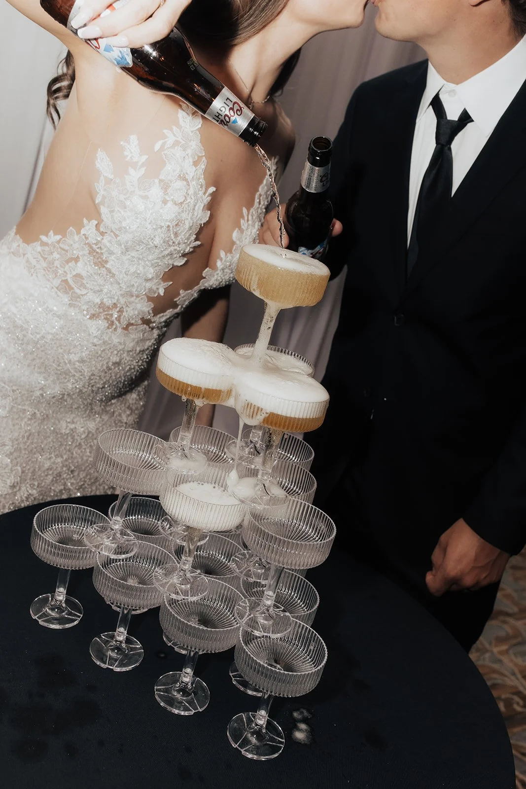 A bride and groom pouring champagne into a pyramid of glasses at a wedding reception.