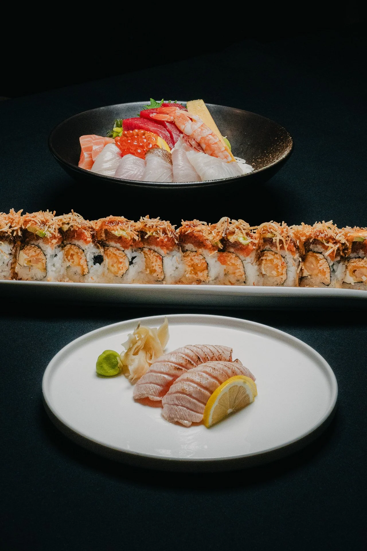 A Japanese meal with sashimi, sushi roll, and a sushi platter on a black table.