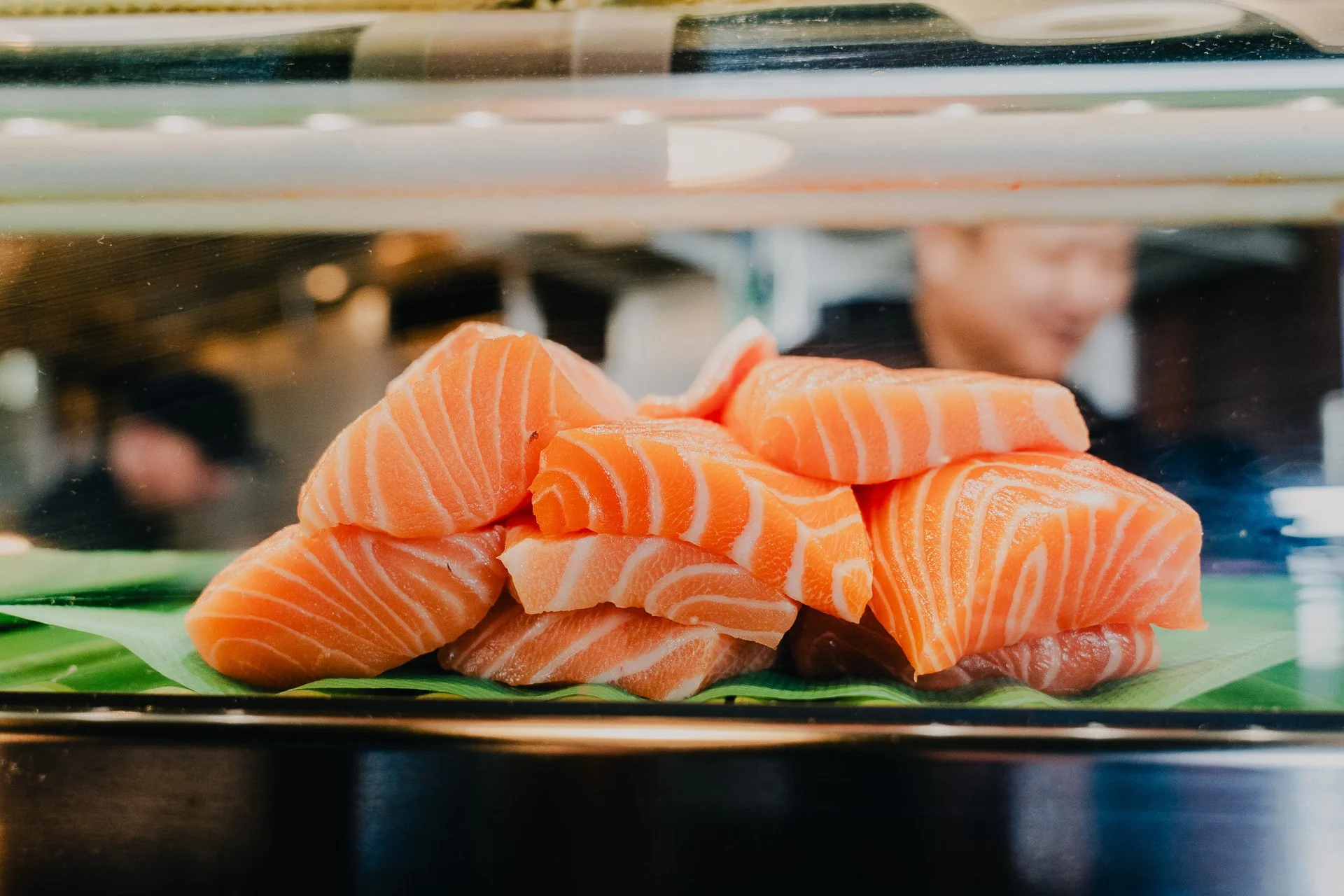 Fresh slices of raw salmon fish displayed on a green leaf at a sushi restaurant.