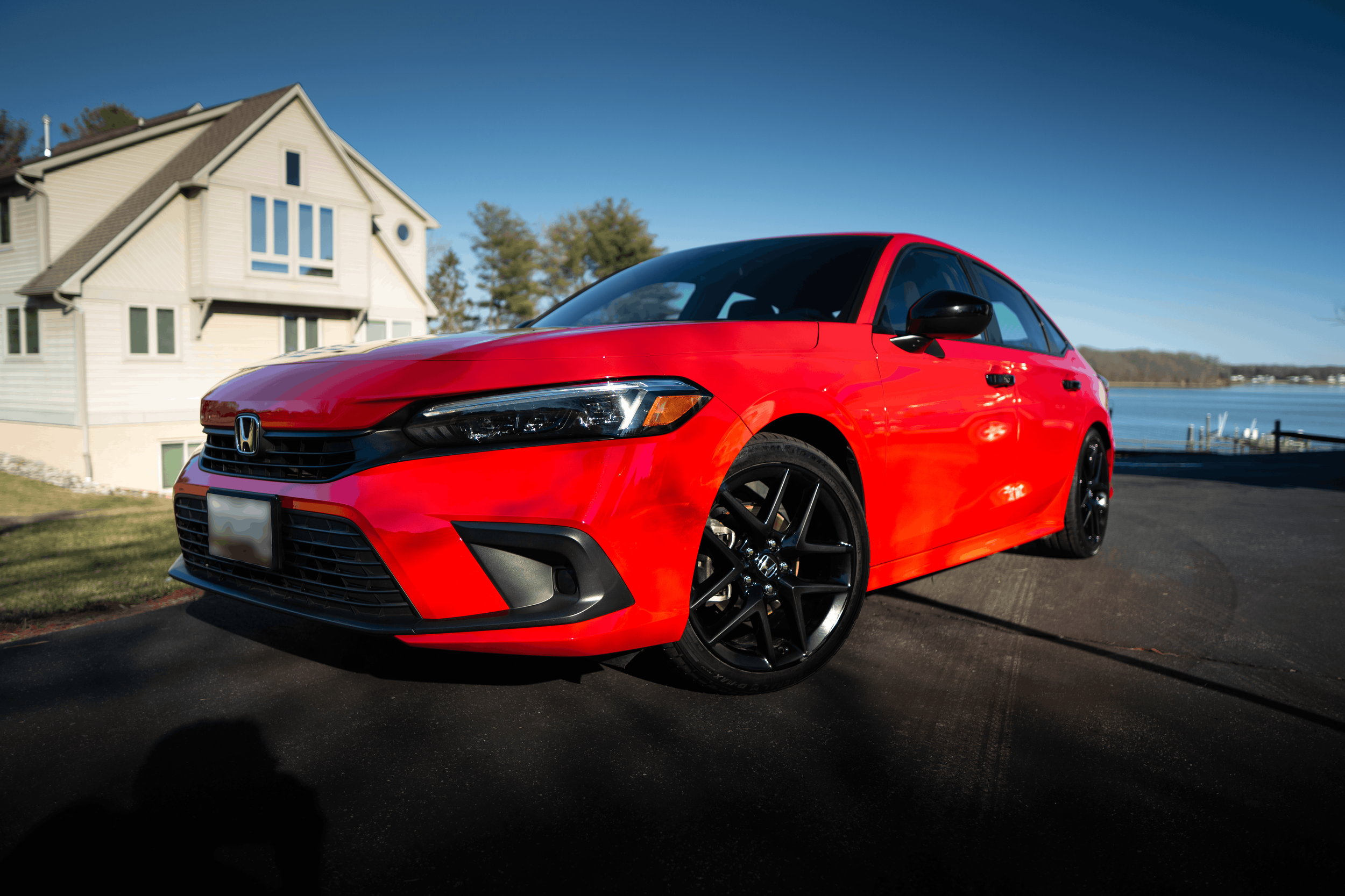 A red Honda Civic parked on a driveway near a house by a body of water on a clear day.