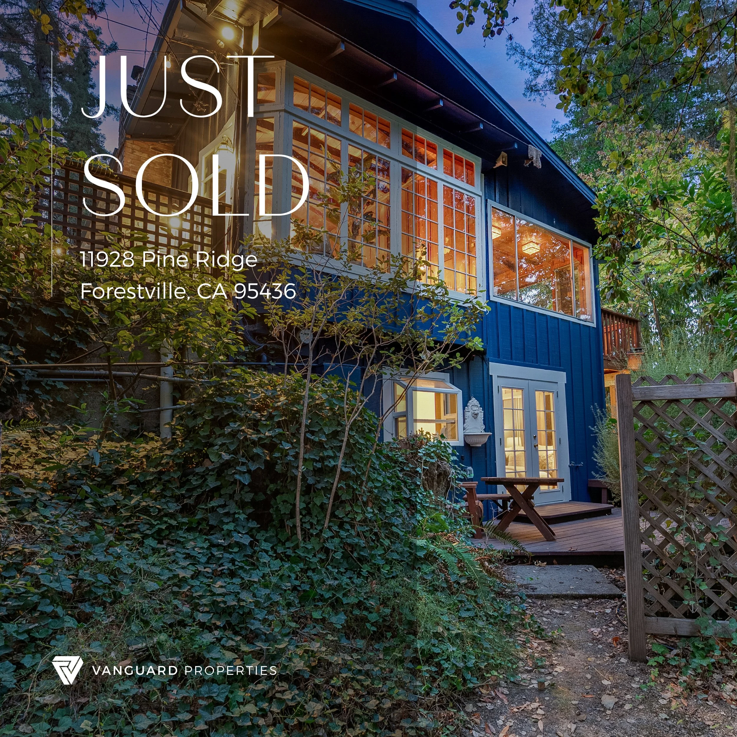 A two-story blue house with large windows illuminated from within, surrounded by trees and greenery, with a small wooden deck and a lattice fence in the front yard. Overlaid text reads 'JUST SOLD' with the address '11928 Pine Ridge, Forestville, CA 9