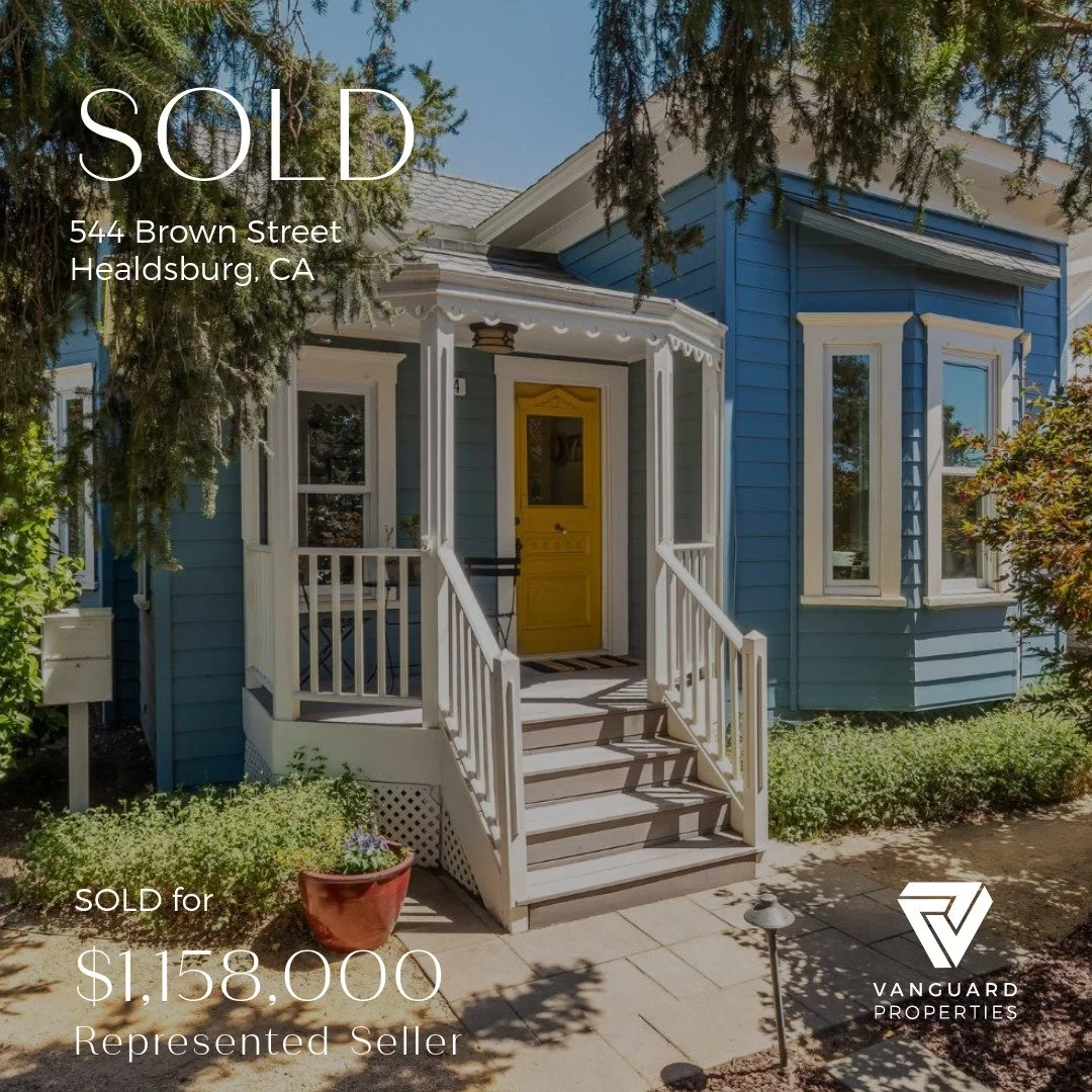 A blue house with a yellow front door and a white porch. Trees and bushes surround the house, with a small pathway leading to the steps. The house has a SOLD banner and information about the property and seller.