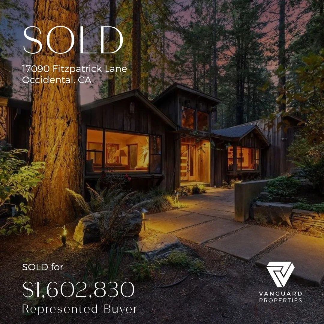 A sold sign overlaying a photo of a dark wood house in a wooded area at sunset with lit windows and a stone pathway.