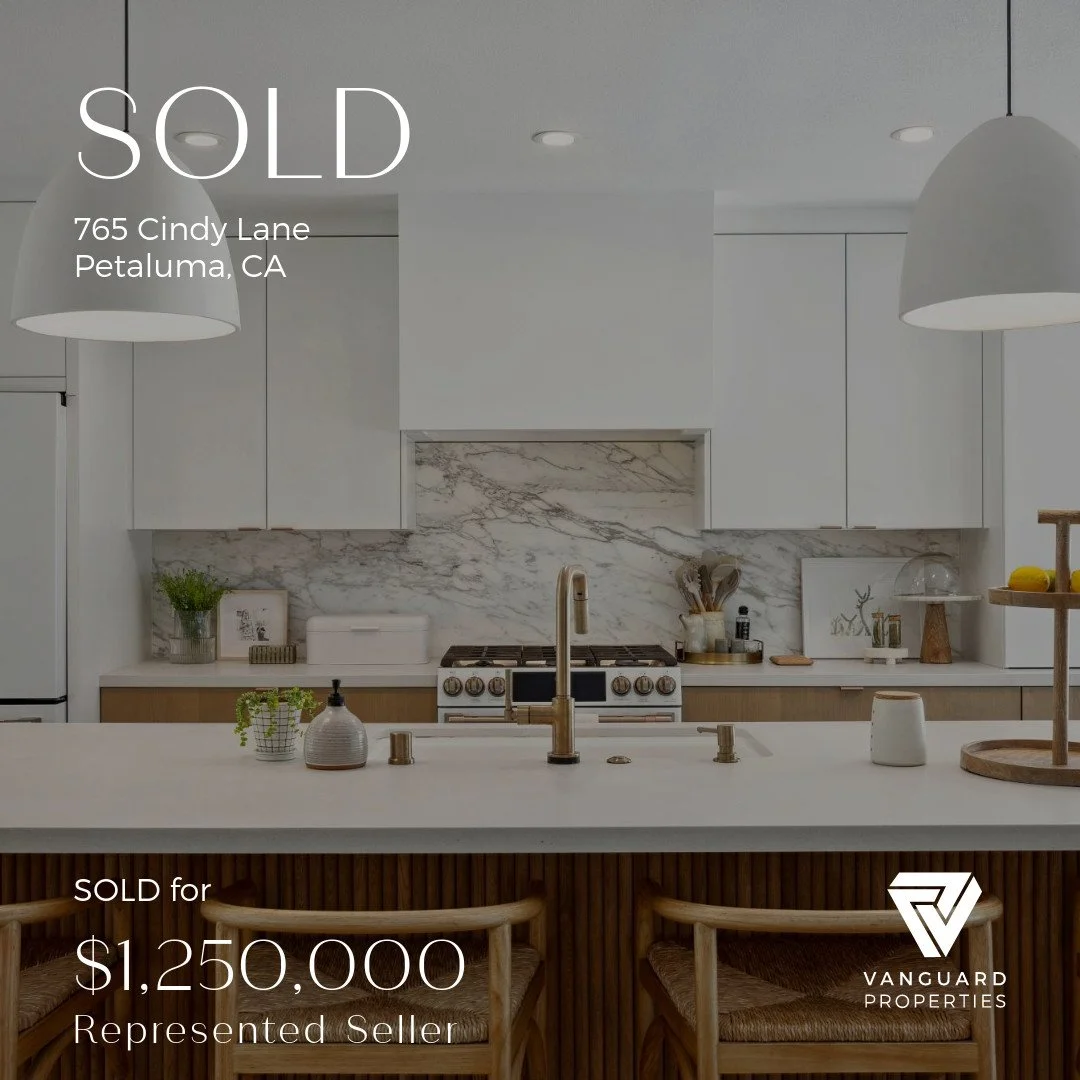 Interior view of a modern kitchen with white cabinetry, marble backsplash, and a central island with seating. Text overlay indicates the property has been sold for $1,250,000 in Petaluma, CA, by Vanguard Properties.