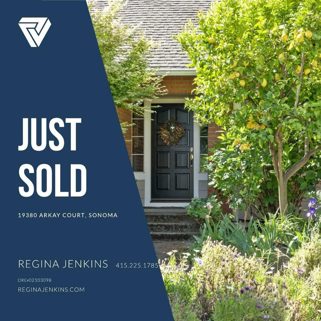 A house with a black front door decorated with a wreath, surrounded by green trees and plants in a garden.