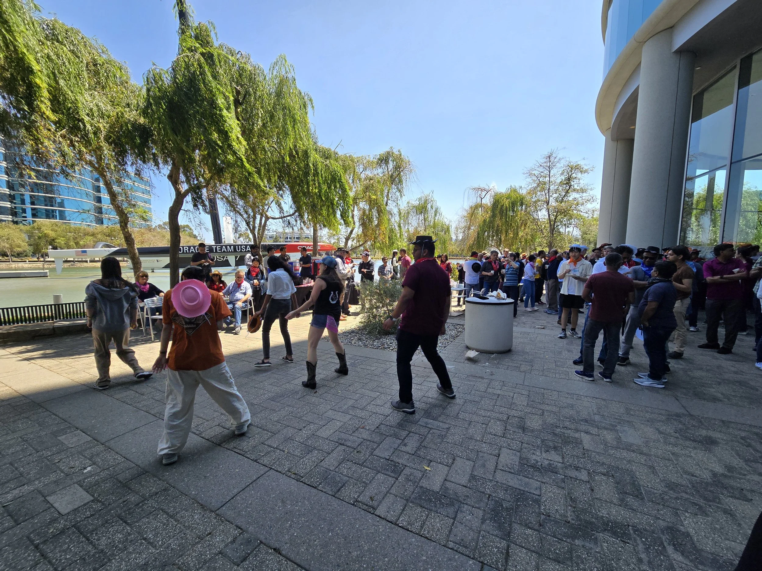 A Corporate Event for Oracle in Redwood Shores featuring a band and Line Dancing Lisa with DJ Shivers. People dancing and chatting under trees, with a boat in the background along a waterway.