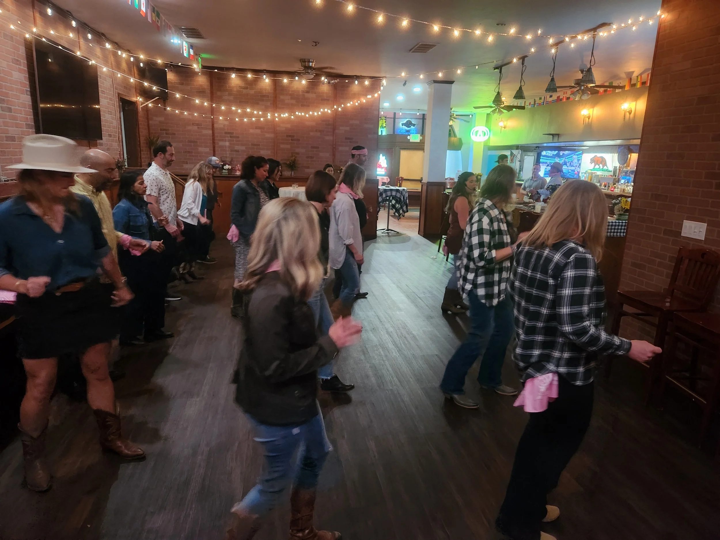 Private event at Lariat Tavern in Belmont by DJ Shivers. People line dancing in a restaurant or bar decorated with string lights, checkered tablecloths, and Western-themed decor.