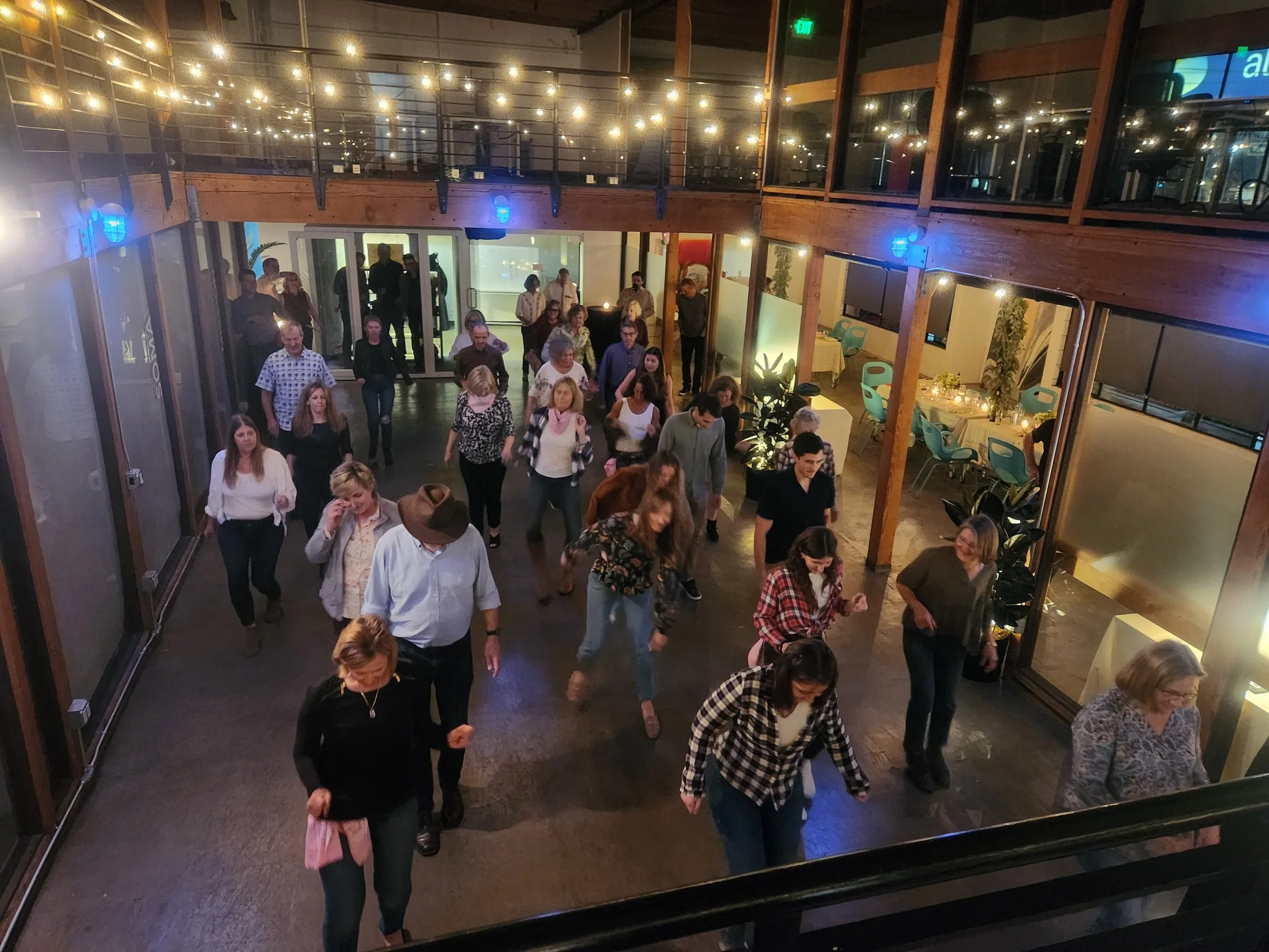 Line Dancing Lisa at a private birthday party event in San Francisco. People dancing in a dimly lit indoor space with string lights overhead, wooden beams, and glass walls.
