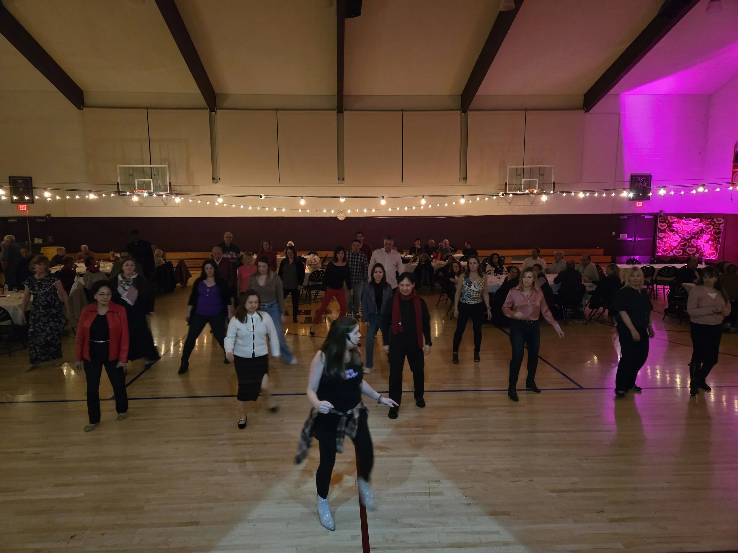 Catholic School Fundraiser private event with DJ Shivers and Line Dancing Lisa. People dancing and socializing in a gymnasium decorated with string lights for a social event