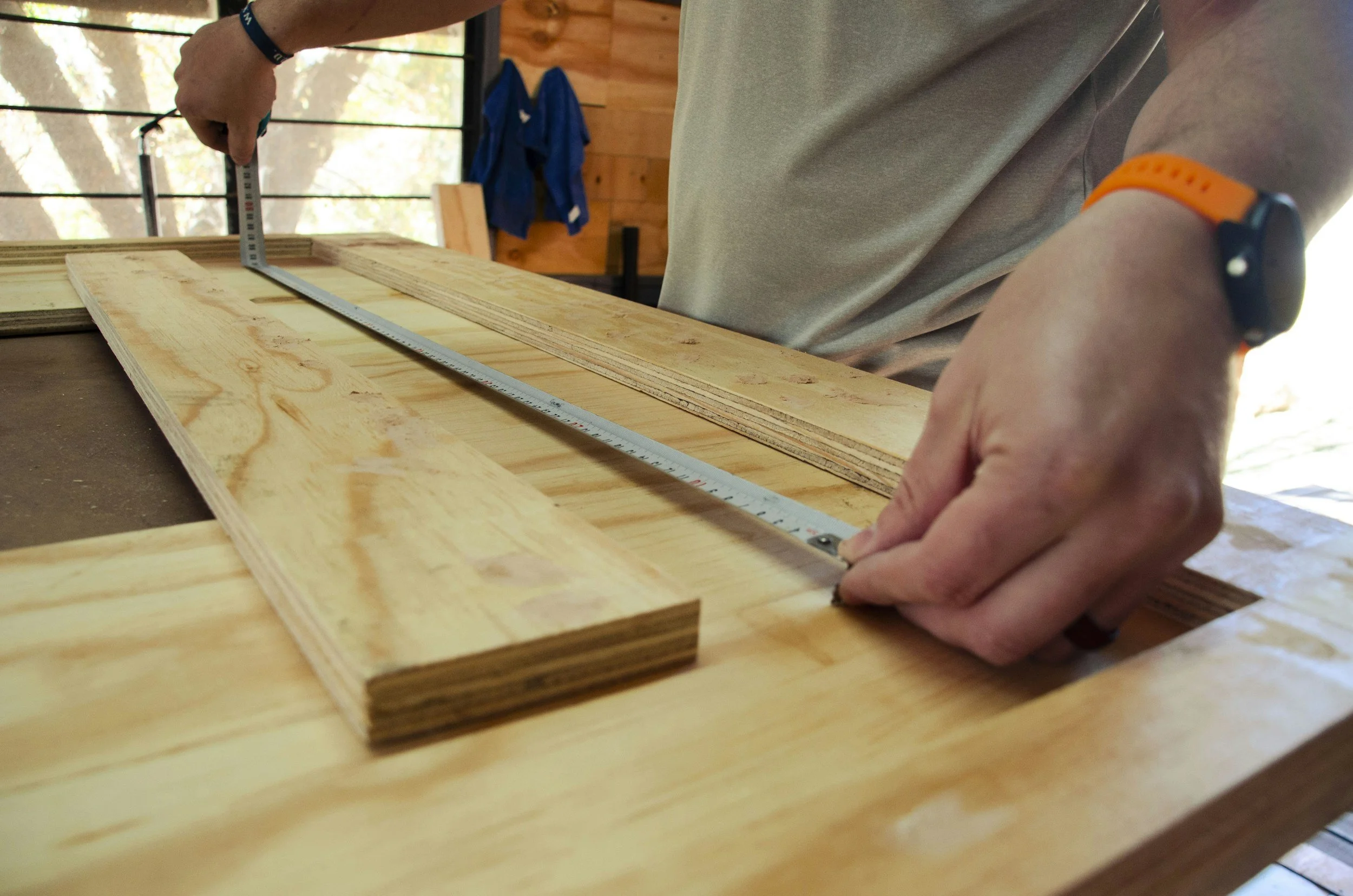 Close-up of a person measuring and marking a wooden board with a metal ruler in a woodworking workshop.