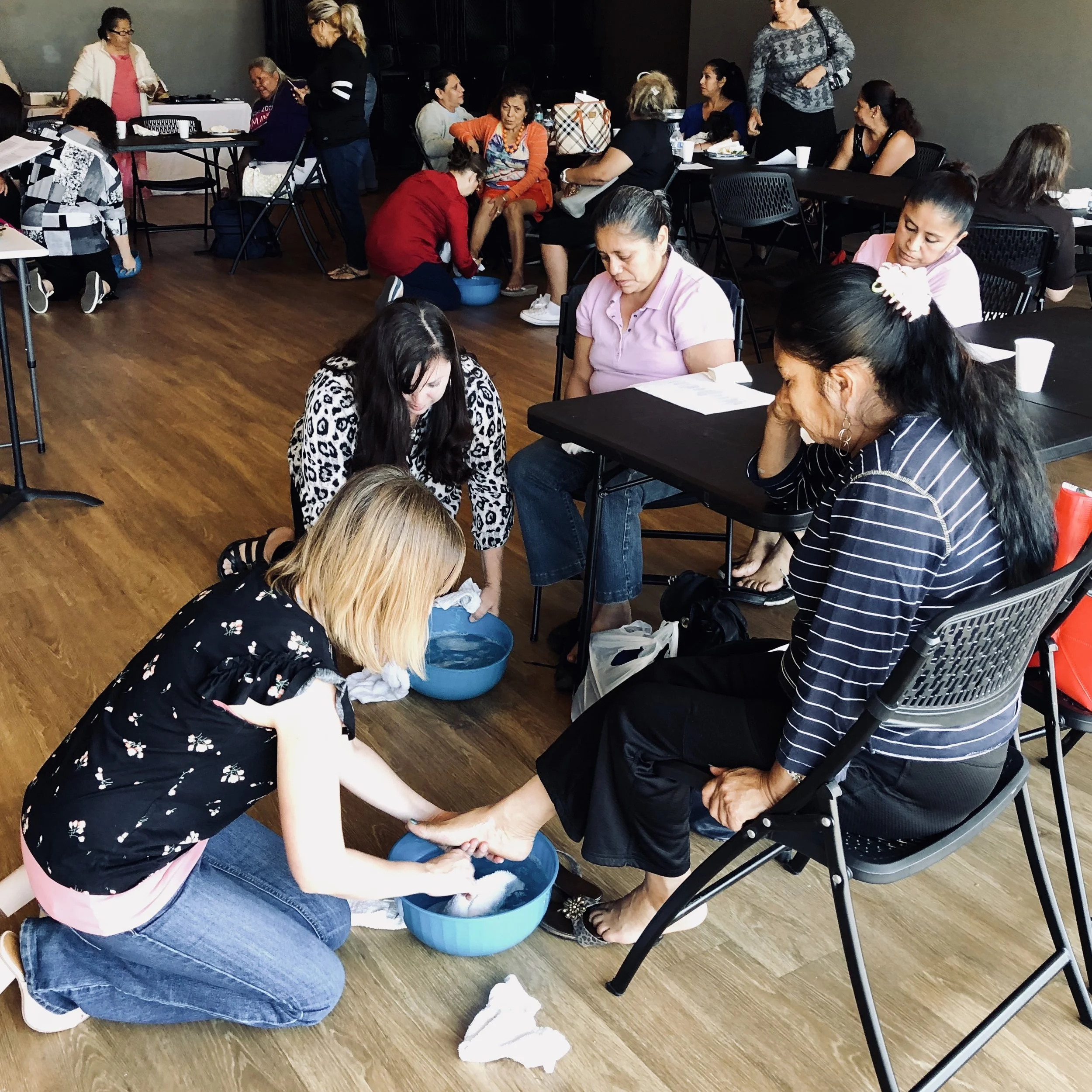 Women receiving foot washing service from volunteers in a community center