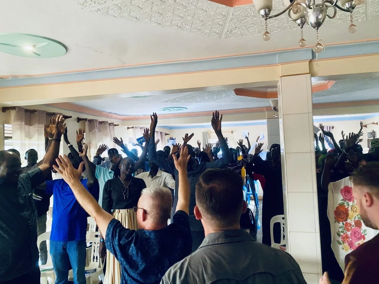A group of people inside a room, raising their hands during a meeting or celebration.