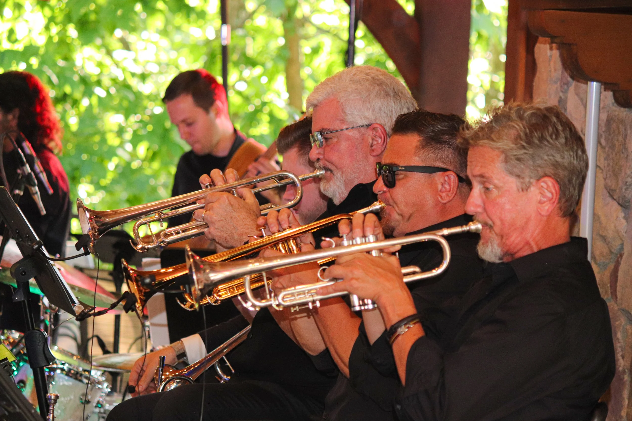 A group of older men playing trumpets during a live outdoor musical performance.