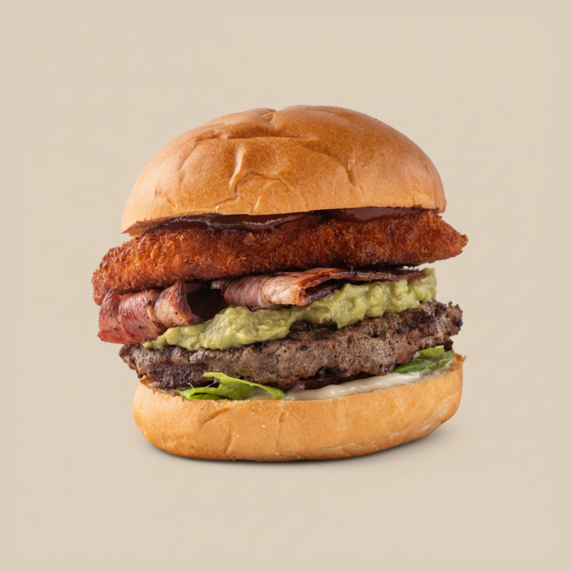A close-up of a gourmet burger with a bun, grilled beef patty, lettuce, mayonnaise, guacamole, bacon, a fried chicken fillet, and barbecue sauce.