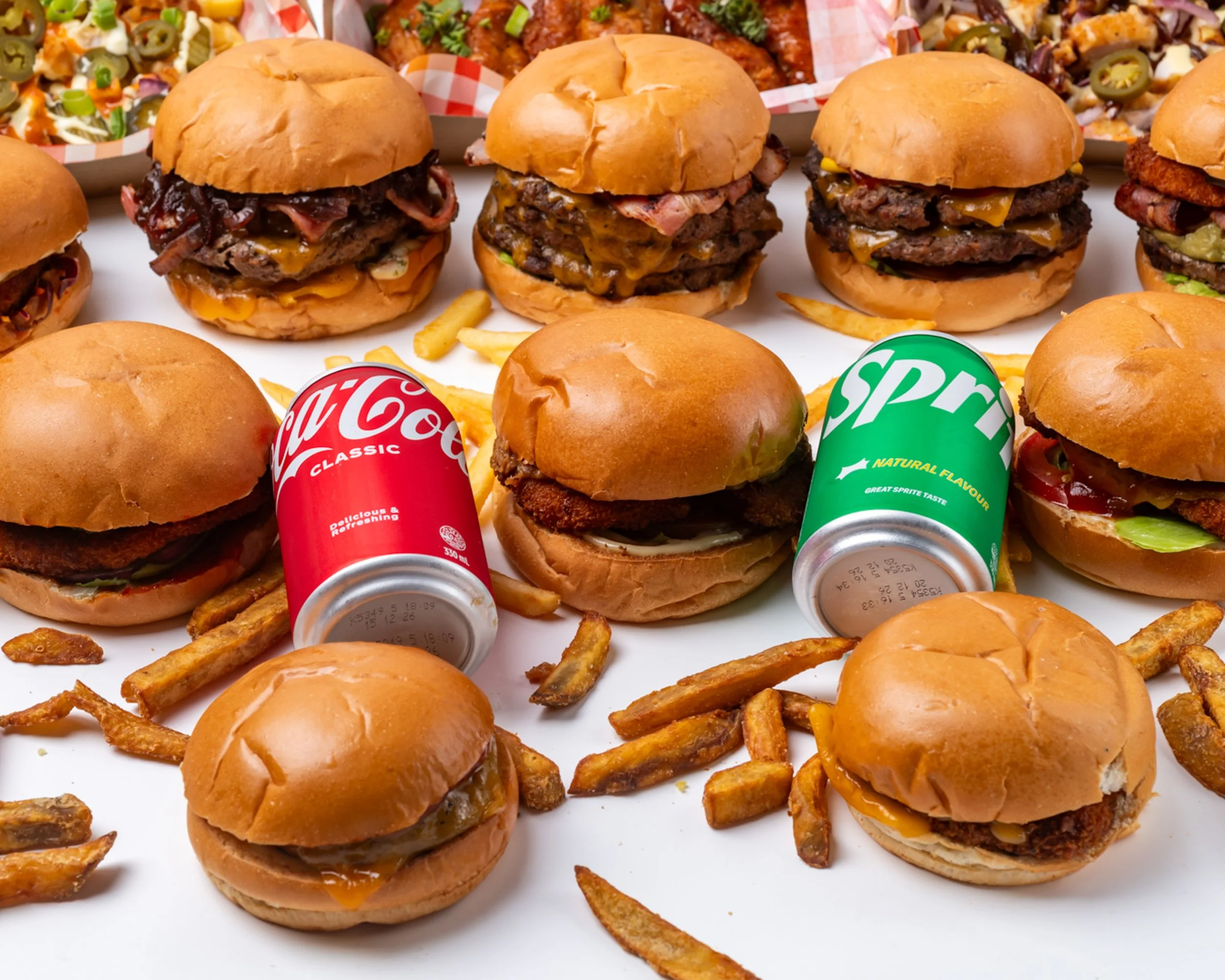 Arrangement of cheeseburgers, French fries, and sodas on a white surface.