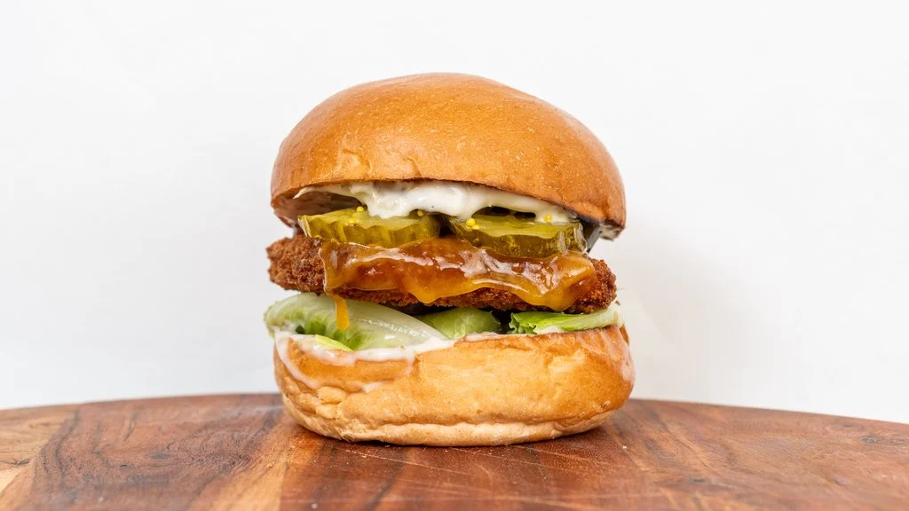 A cheeseburger with pickles, lettuce, tomato, and condiments on a bun, placed on a wooden surface.
