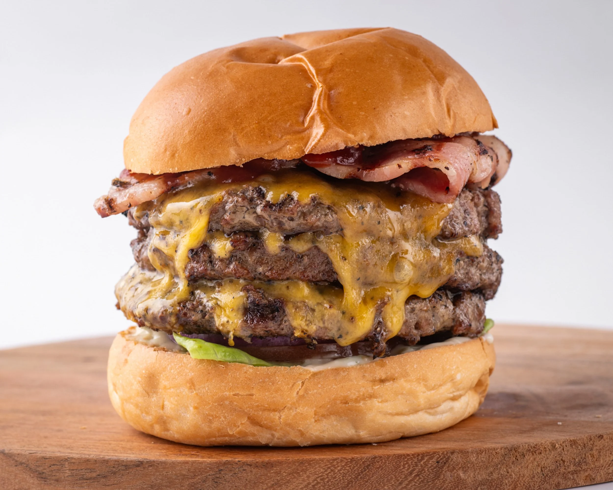 A cheeseburger with bacon in a bun on a wooden surface.