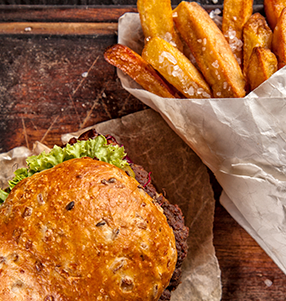 A burger with lettuce and a toasted bun next to a basket of French fries on a wooden surface.