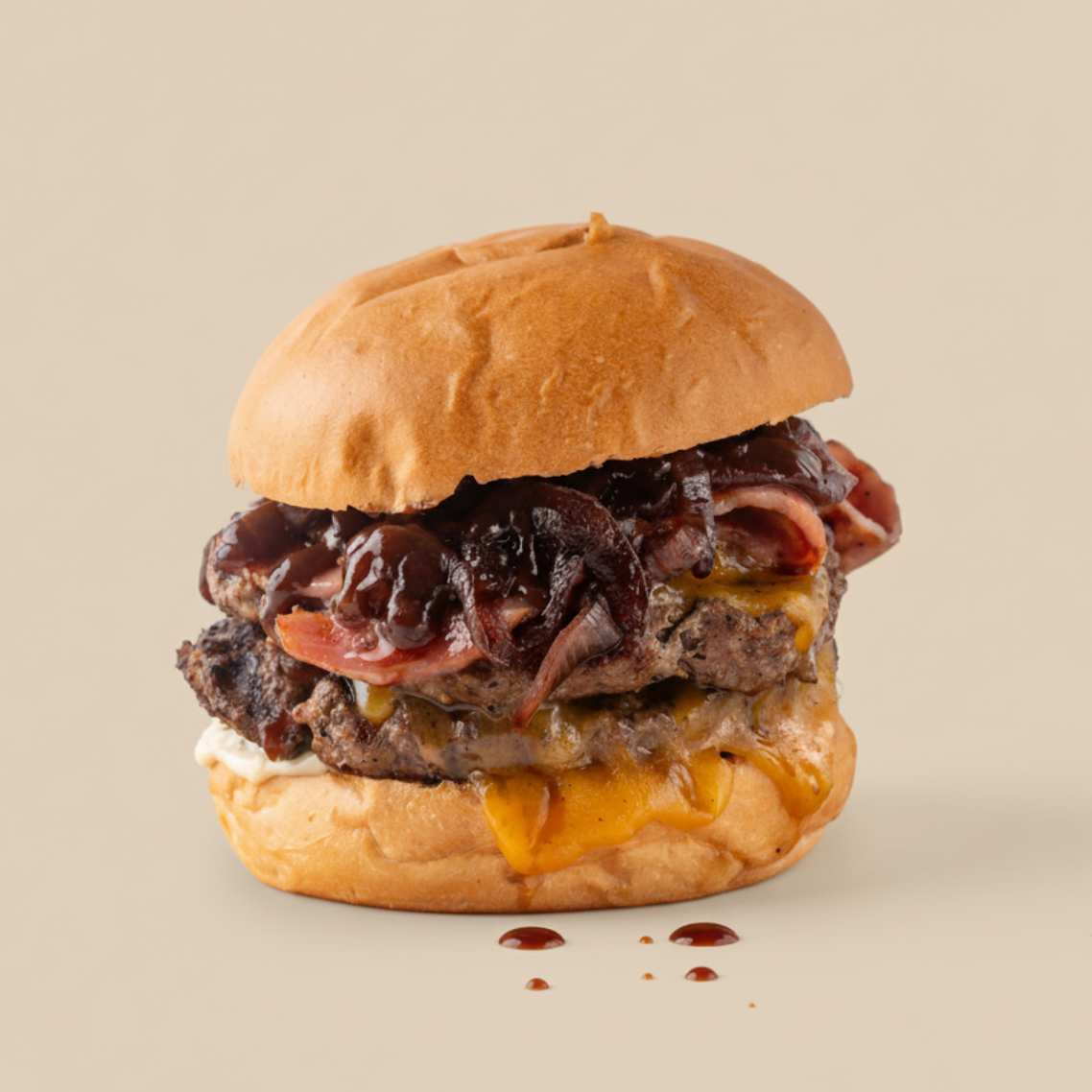 Close-up of a burger with cheese, grilled beef patty, caramelized onions, bacon, and barbecue sauce in a bun on a plain background.