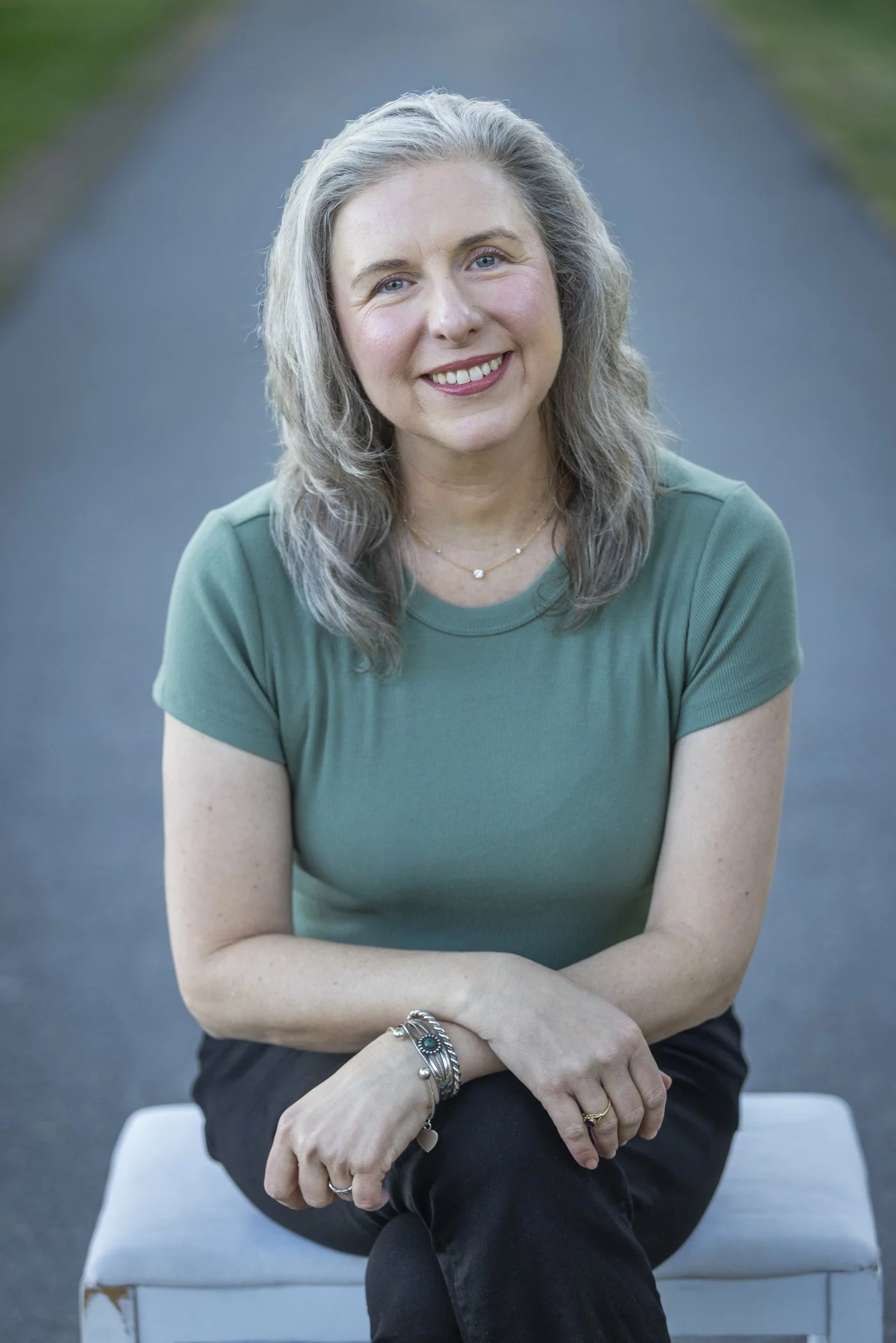 Dr. Teresa Matazzoni sitting outdoors on a bench, wearing a green shirt and black pants, smiling at the camera.