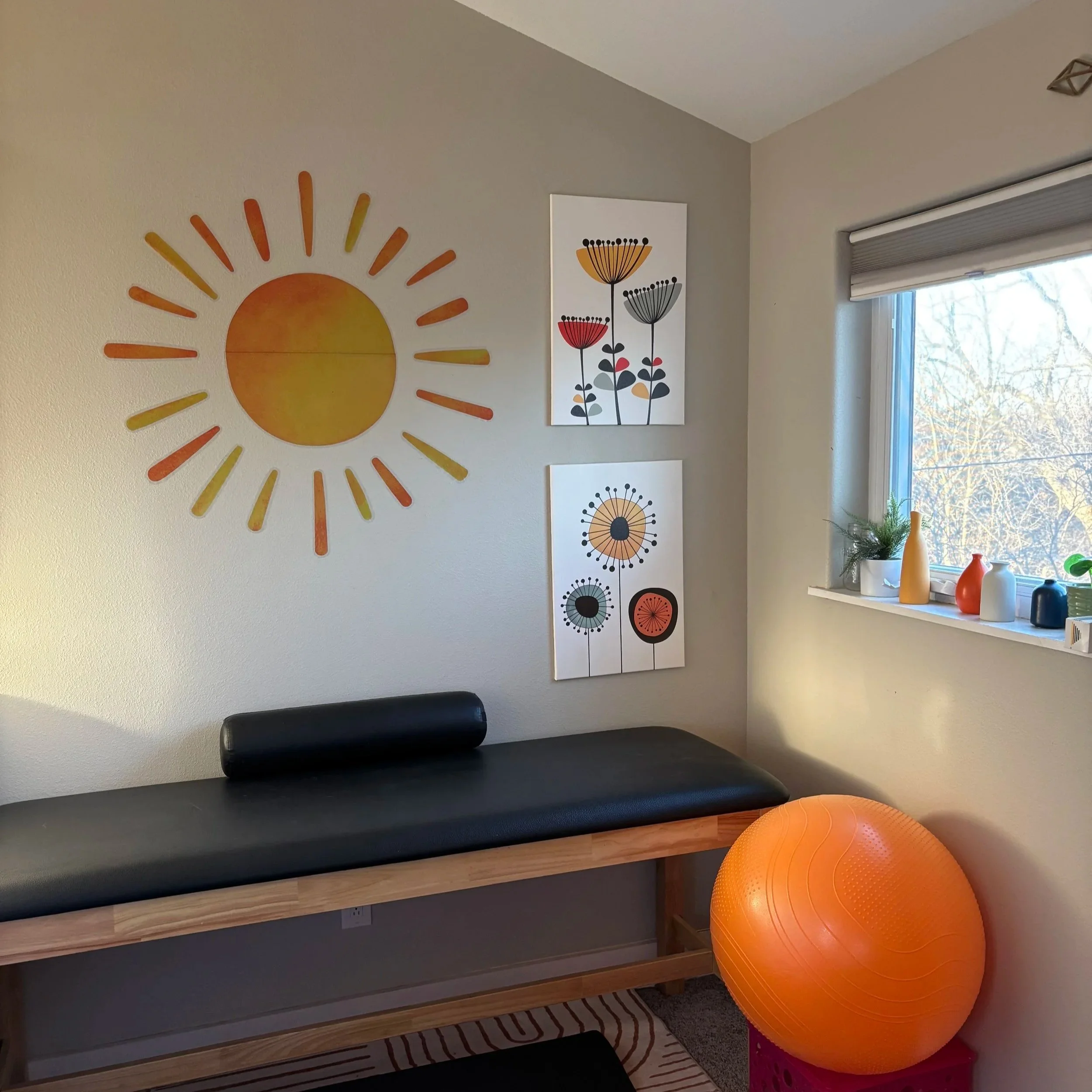 Decorative room corner with wall art, a window with vases on the sill, and an exercise ball.