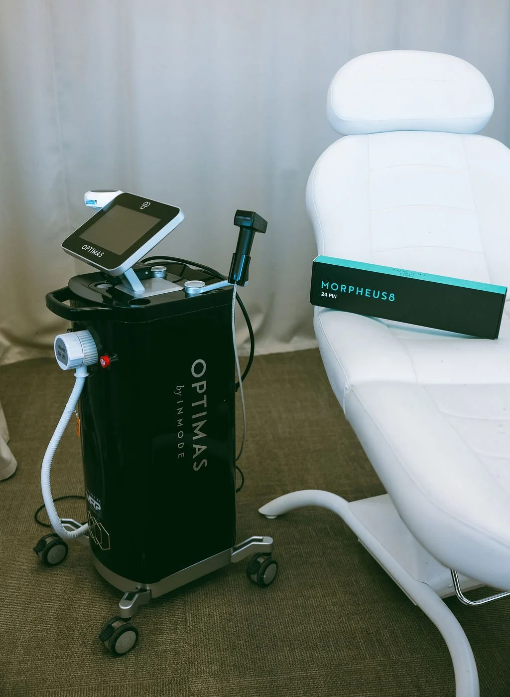 Medical equipment cart beside a white examination chair with a box labeled 'Morpheus8 24 PIN' on the chair.
