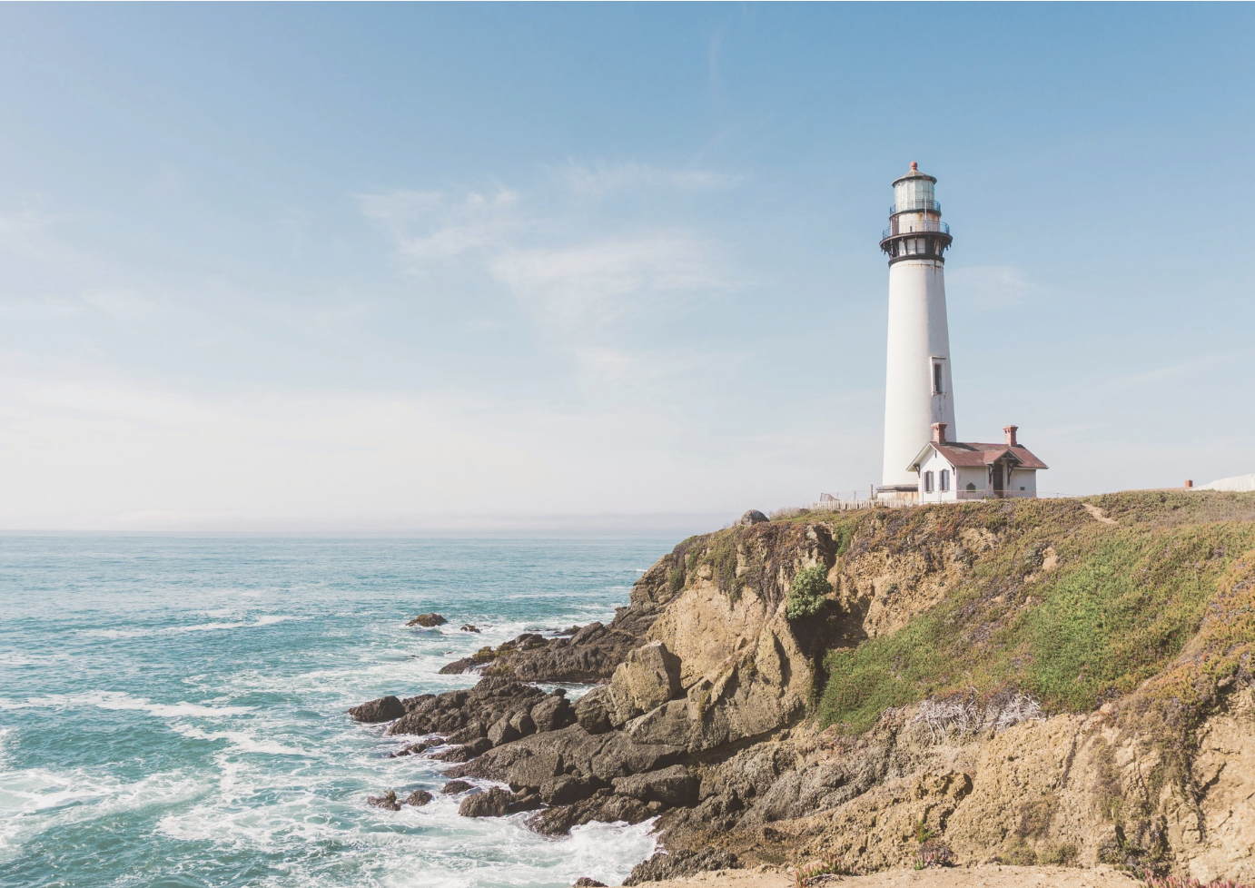 A lighthouse situated on a rocky coastline with an ocean view and a clear blue sky.